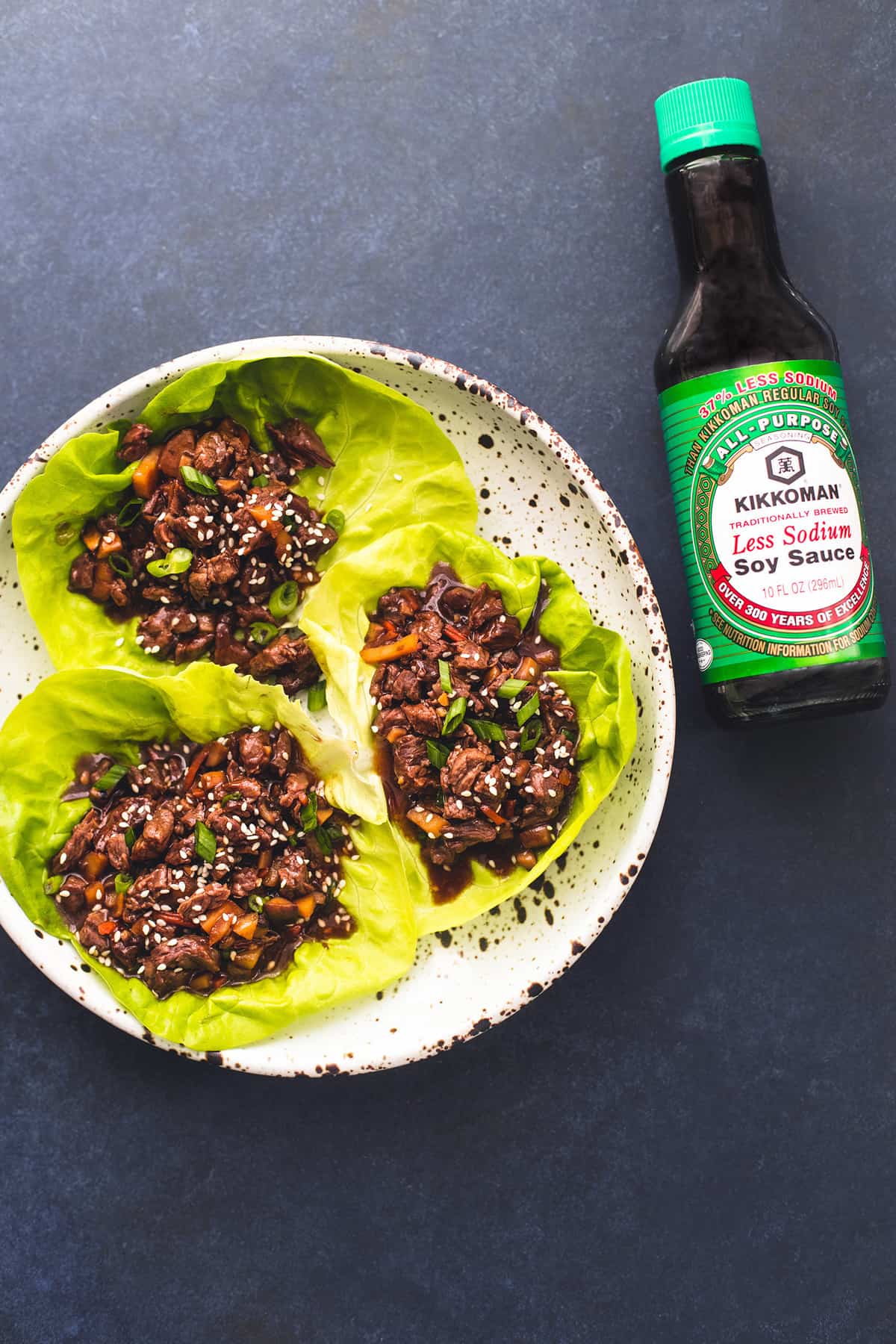 top view of honey beef lettuce wraps on a plate with a bottle of Kikkoman soy sauce on the side.