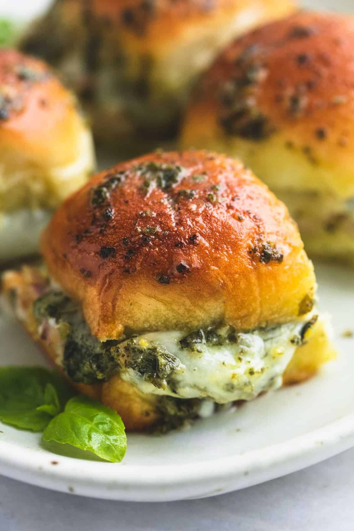 a pesto mozzarella chicken slider with more sliders in the background on a plate.