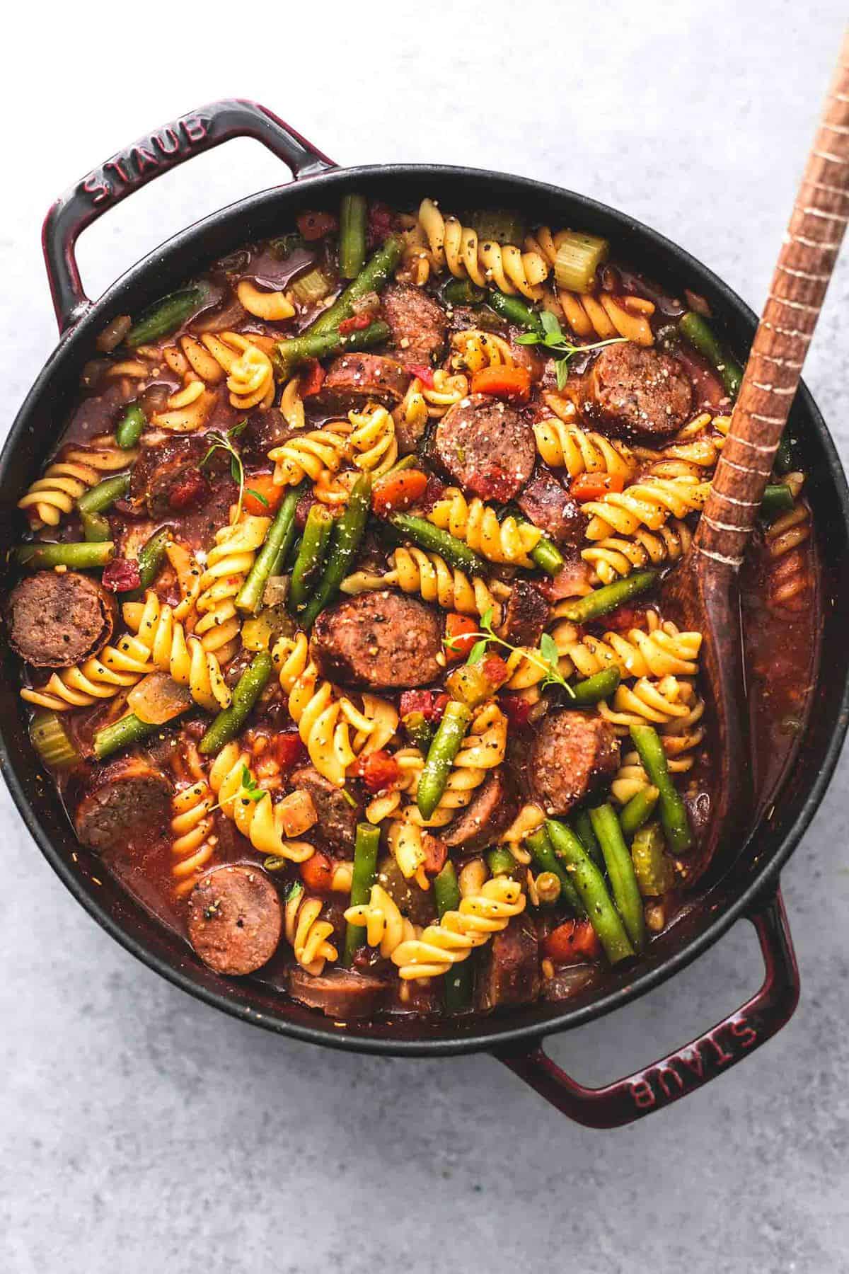 top view of sausage and vegetable soup with a wooden serving spoon in a pan.