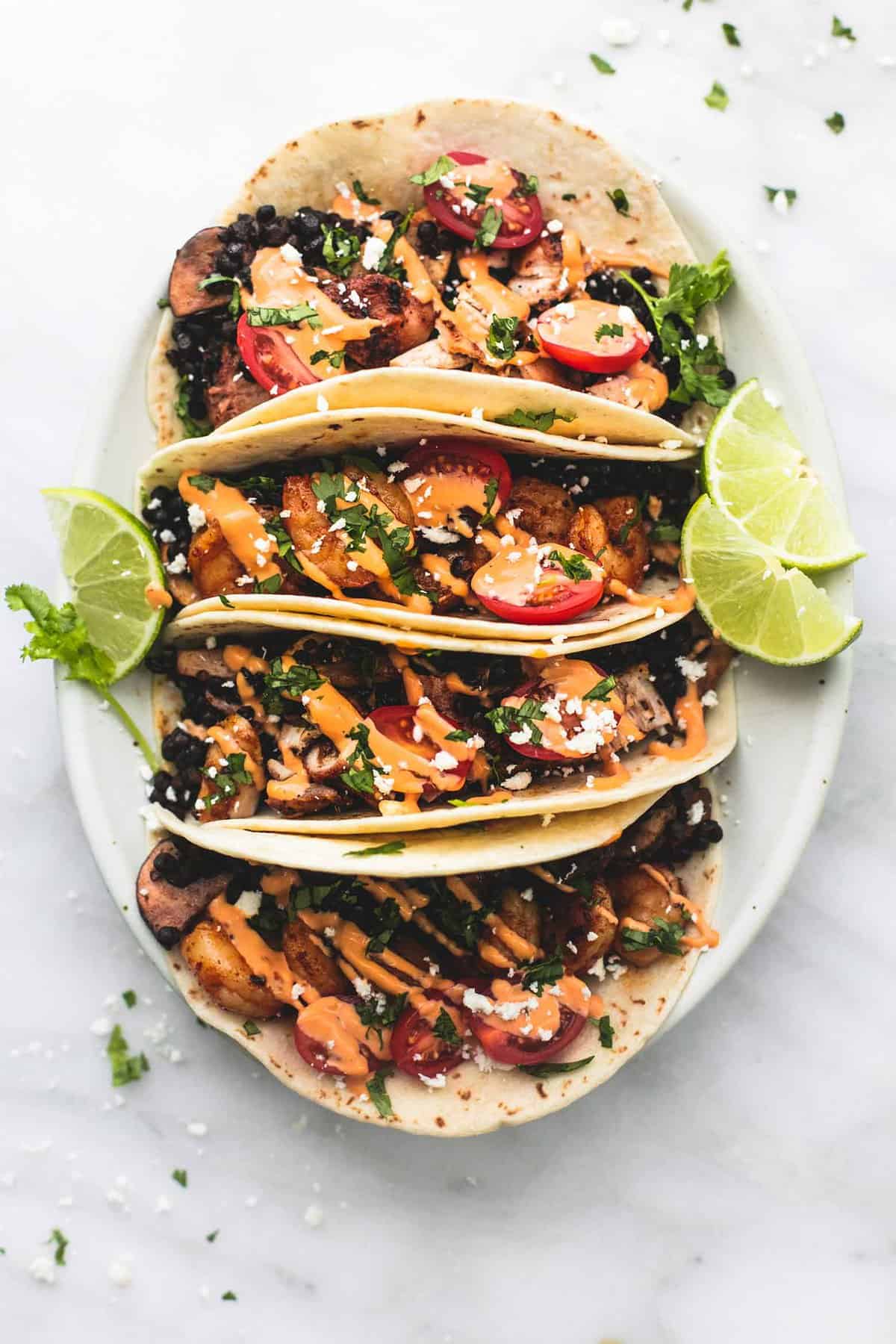 top view of shrimp or chicken and lentil tacos with lime slices on a plate.