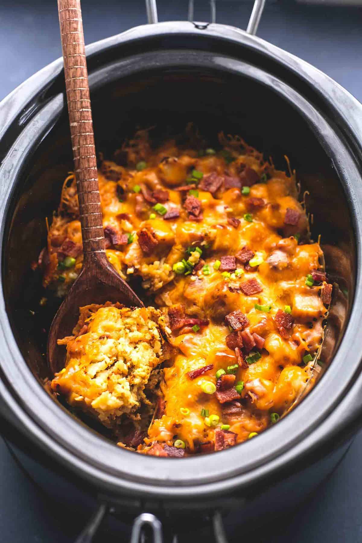 slow cooker loaded tater tot breakfast casserole with a wooden serving spoon in a slow cooker.