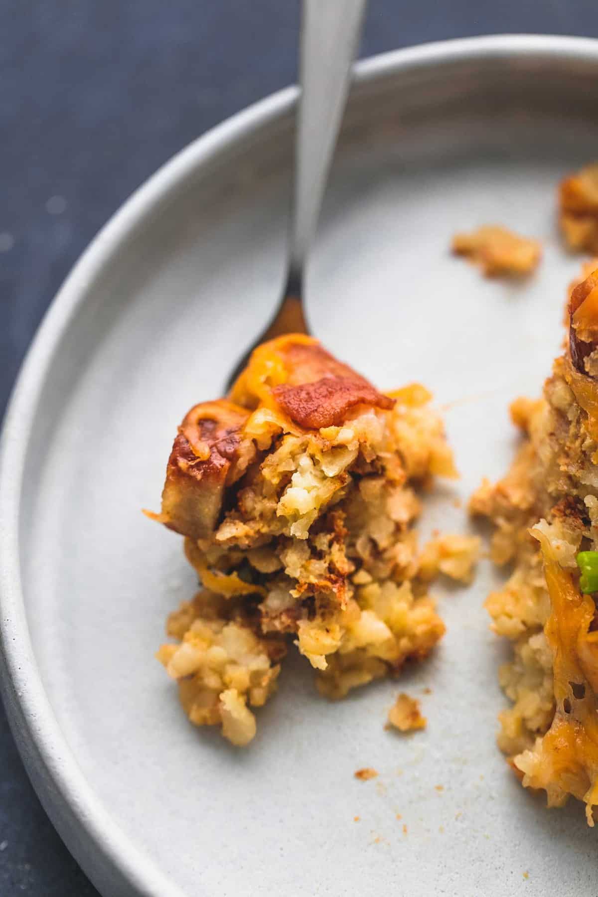 a bite of slow cooker loaded tater tot breakfast casserole on a fork with more on the side all on a plate.
