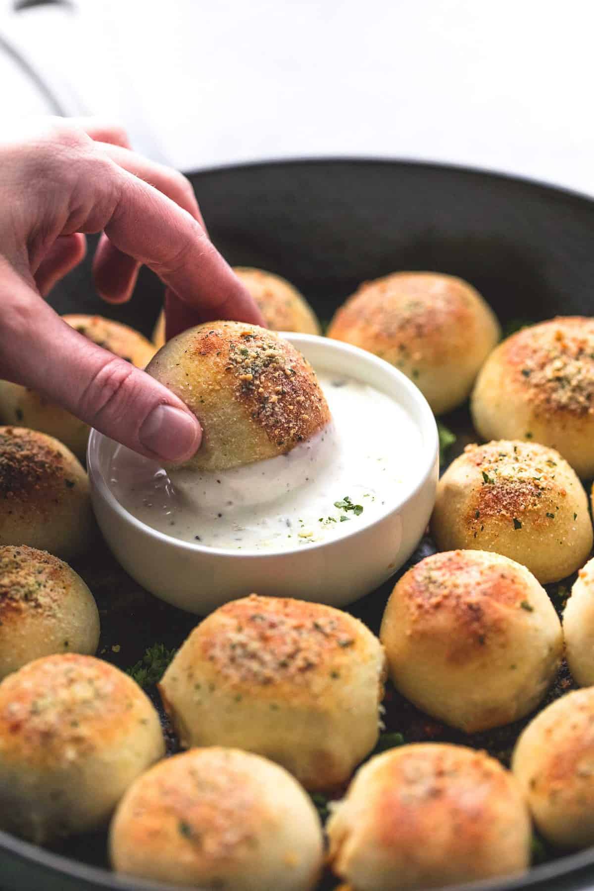 close up of a hand dipping a bbq chicken bite in a bowl of dipping sauce with more bites surrounding it.