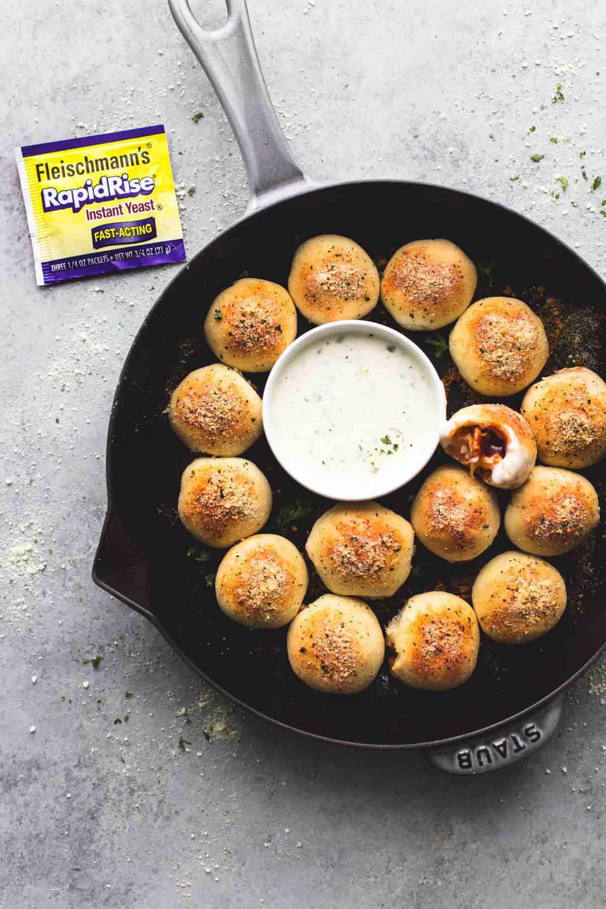 top view of bbq chicken bites with one missing a bite surrounding a bowl of dipping sauce all in a pan with a RapidRise yeast packet on the side.