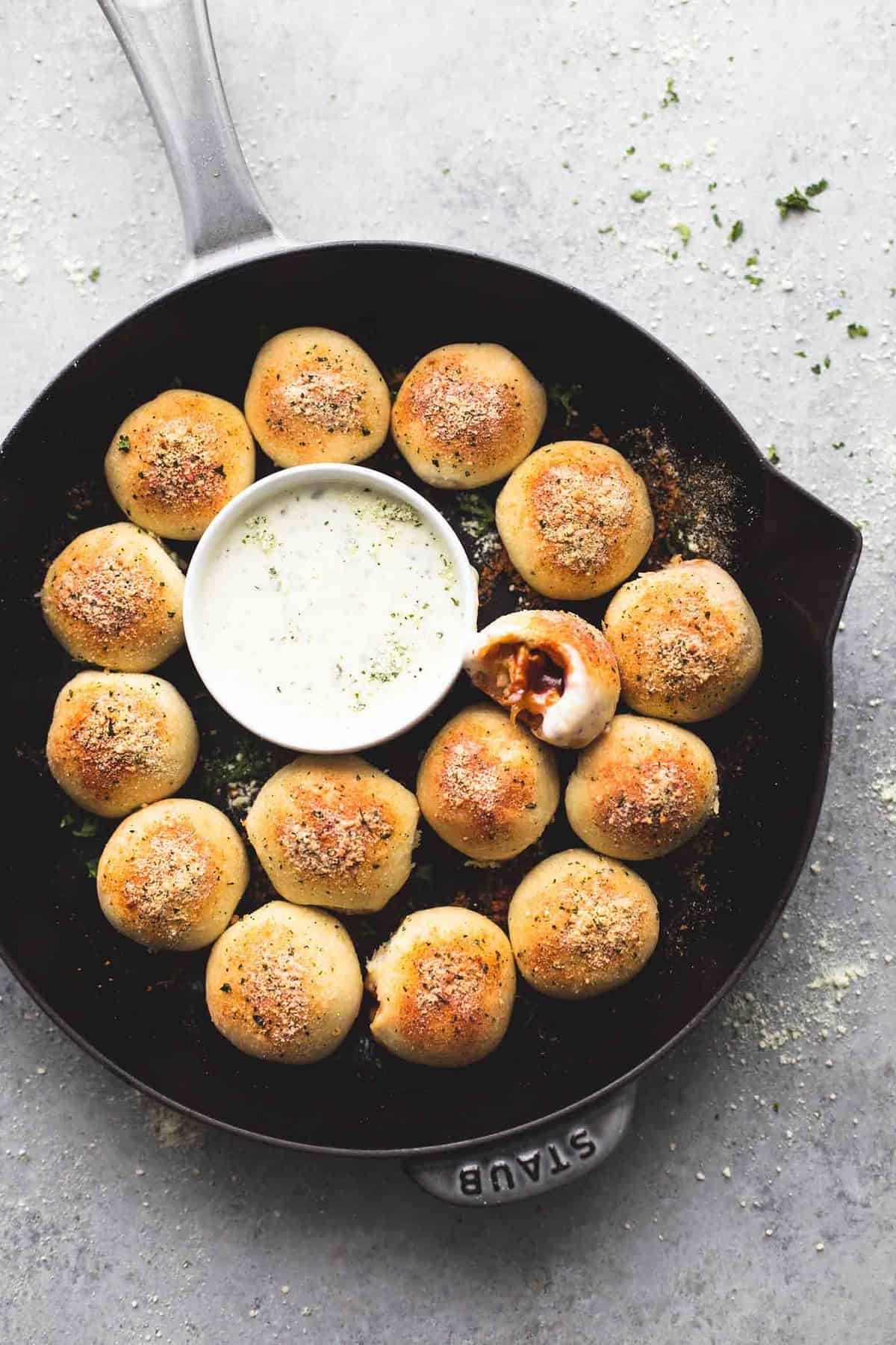 top view of bbq chicken bites with one missing a bite surrounding a bowl of dipping sauce all in a pan.