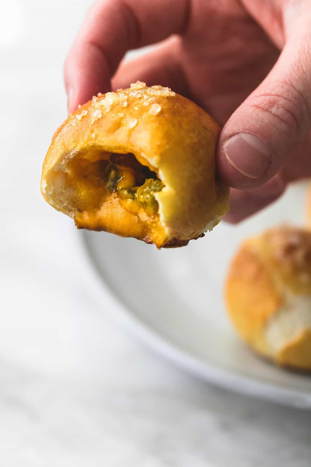 a hand holding a cheddar jalapeño pretzel bite with a bite missing.