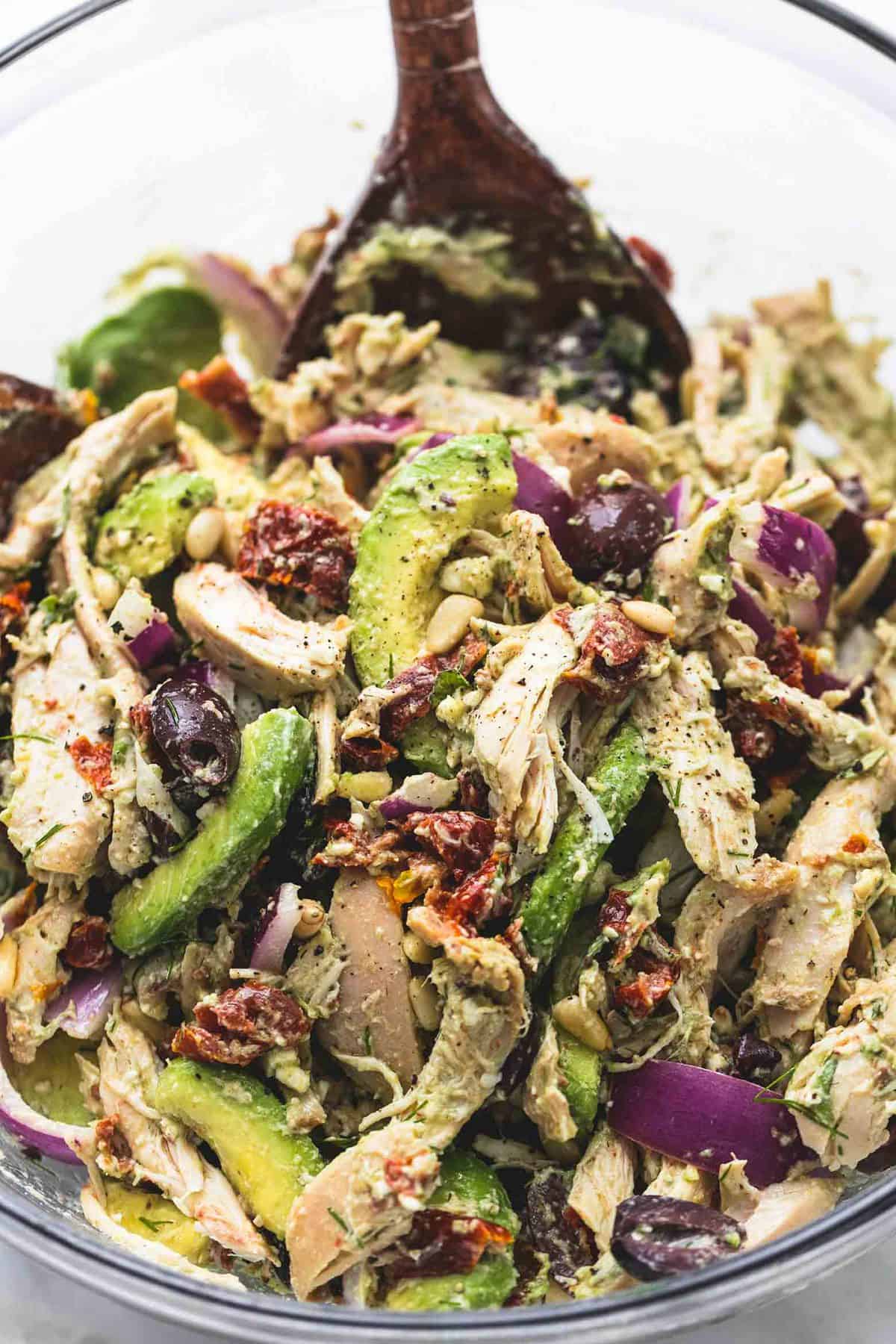 close up of Greek avocado chicken salad with a wooden serving spoon in a glass bowl.