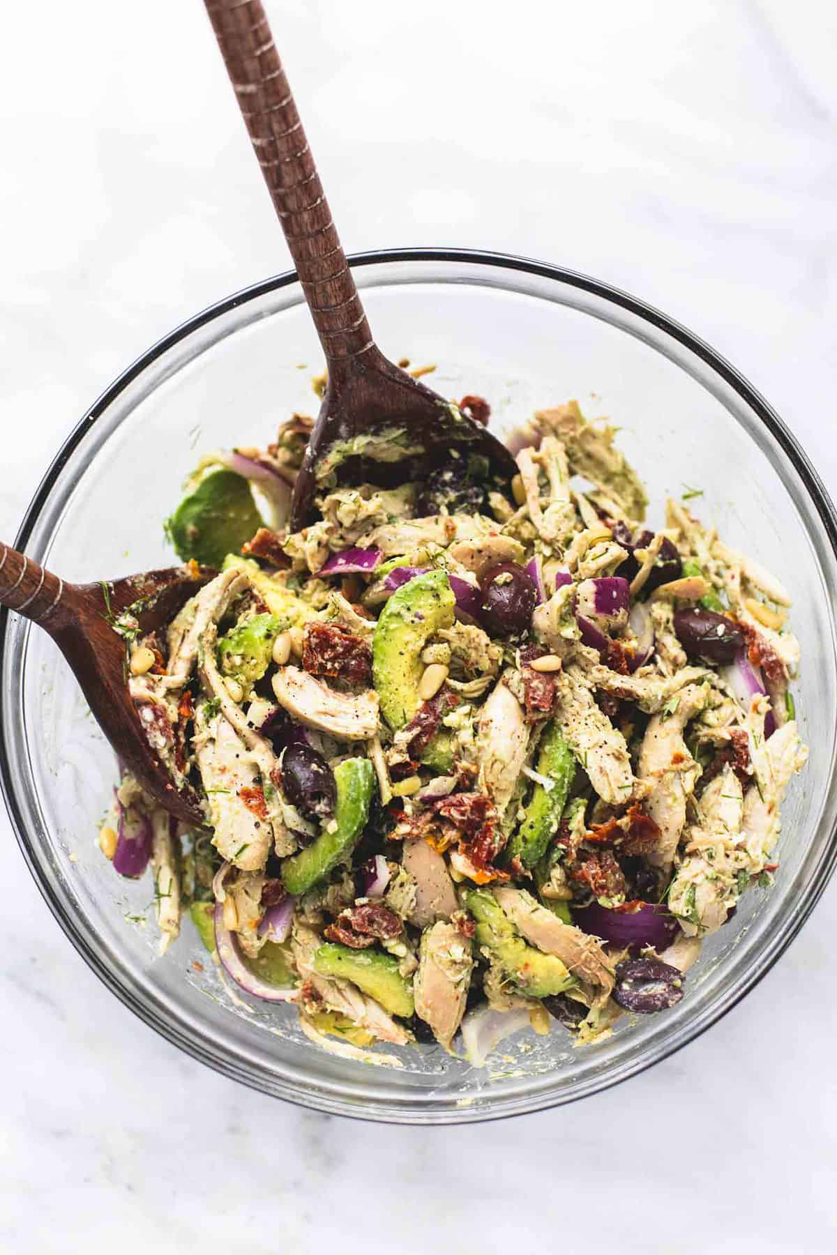 top view of Greek avocado chicken salad with two wooden serving spoons in a glass bowl.