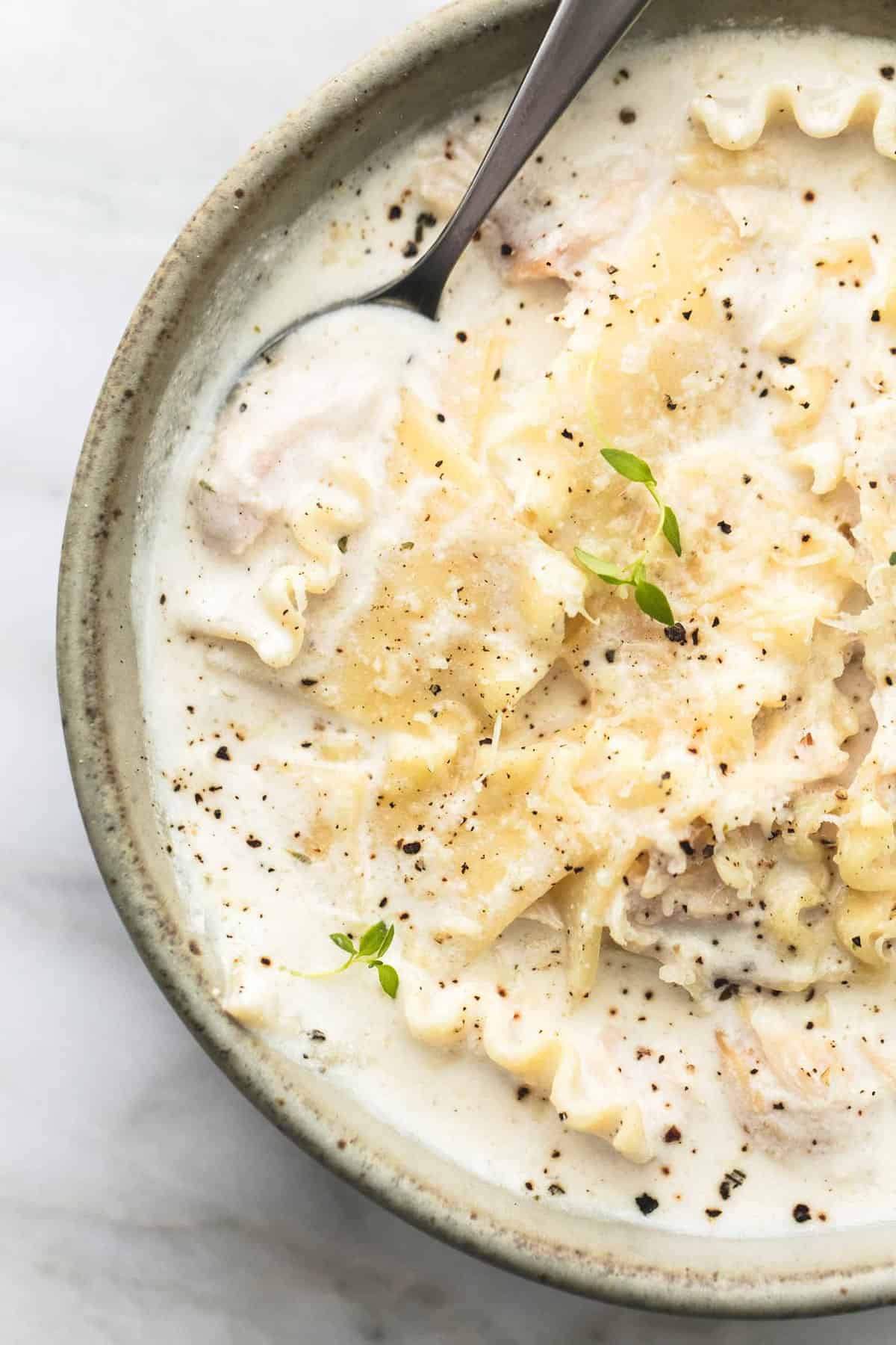 close up top view of creamy white chicken lasagna soup with a spoon in a bowl.