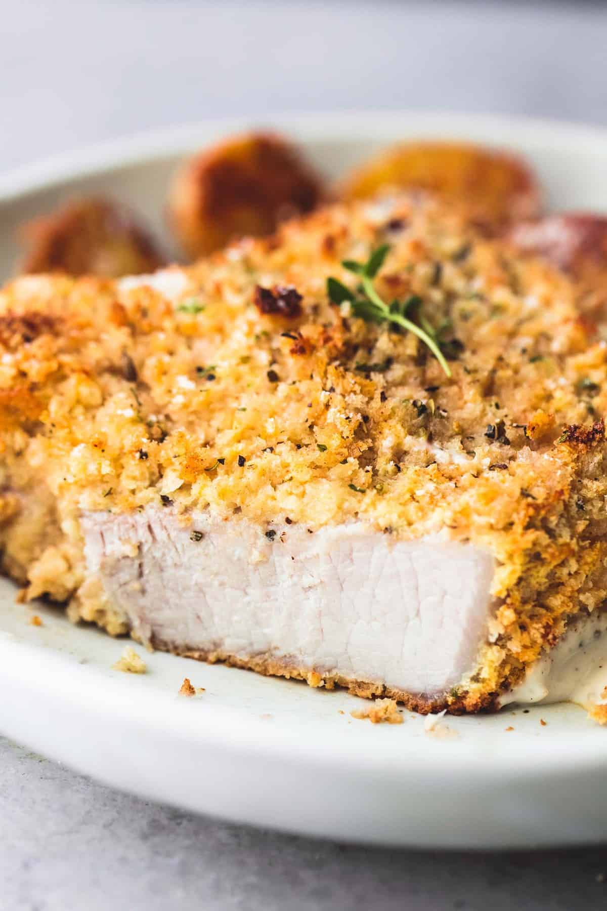 close up of a shake and bake ranch pork chop with a bite missing and potatoes in the background all on a plate.