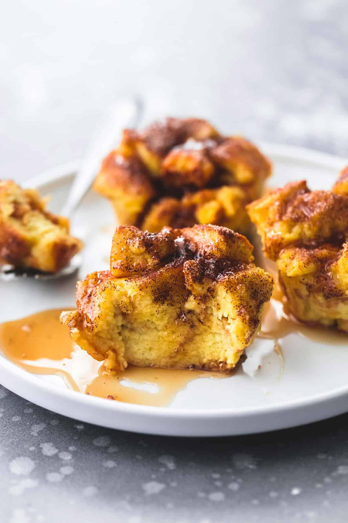 baked cinnamon French toast muffins topped with syrup on a plate with the front one missing a bite and the bite sitting on a fork by the other muffins on the plate.