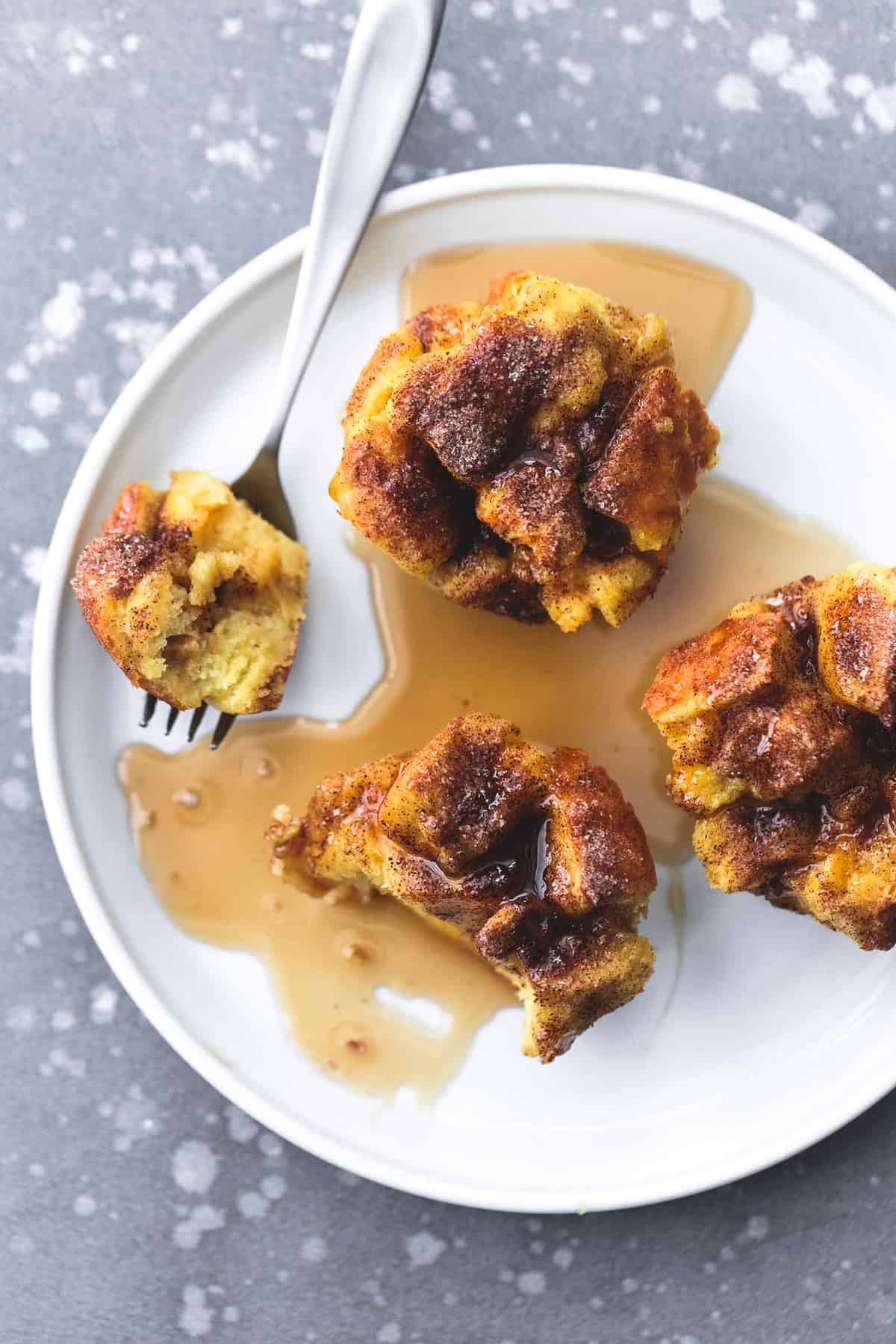 top view of baked cinnamon French toast muffins topped with syrup with a bite missing from one of the muffins with a fork on the side with the bite on top.