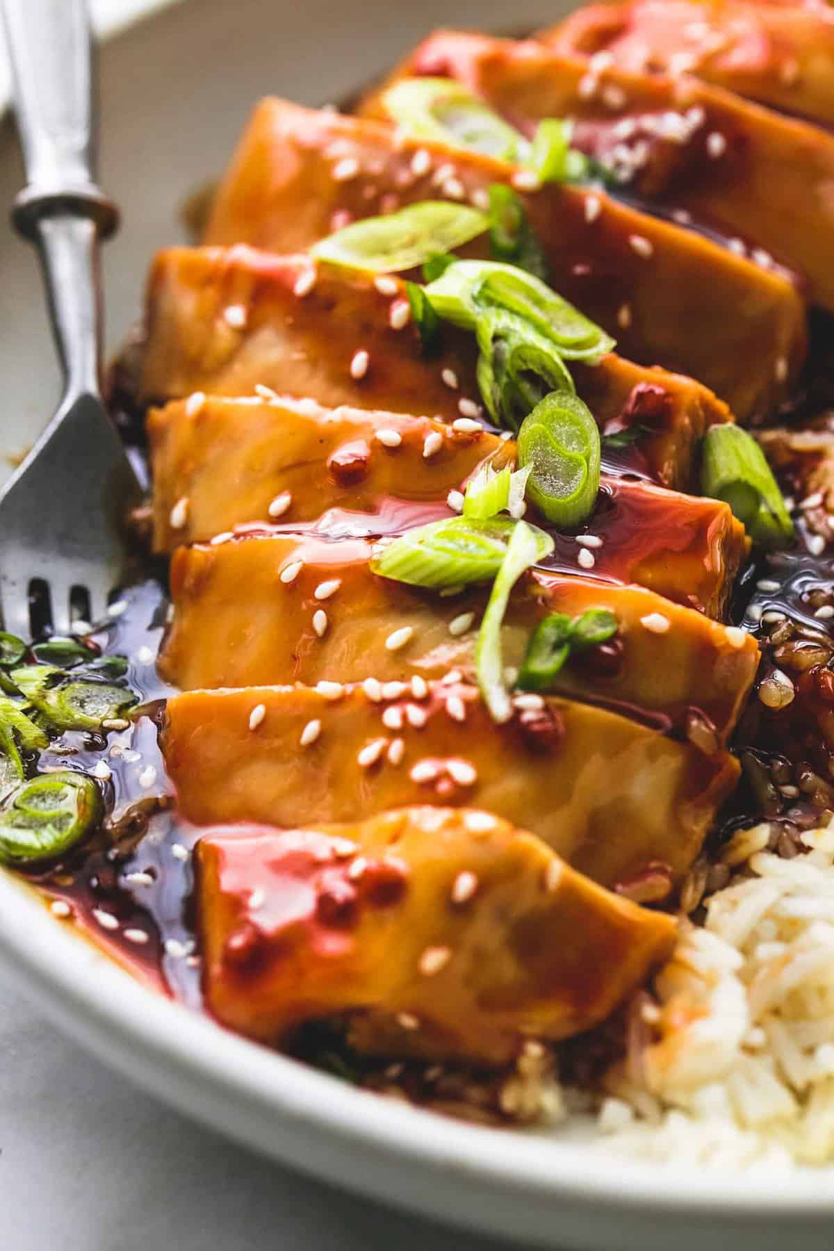 close up of baked teriyaki chicken with a fork and rice on the sides all on a plate.