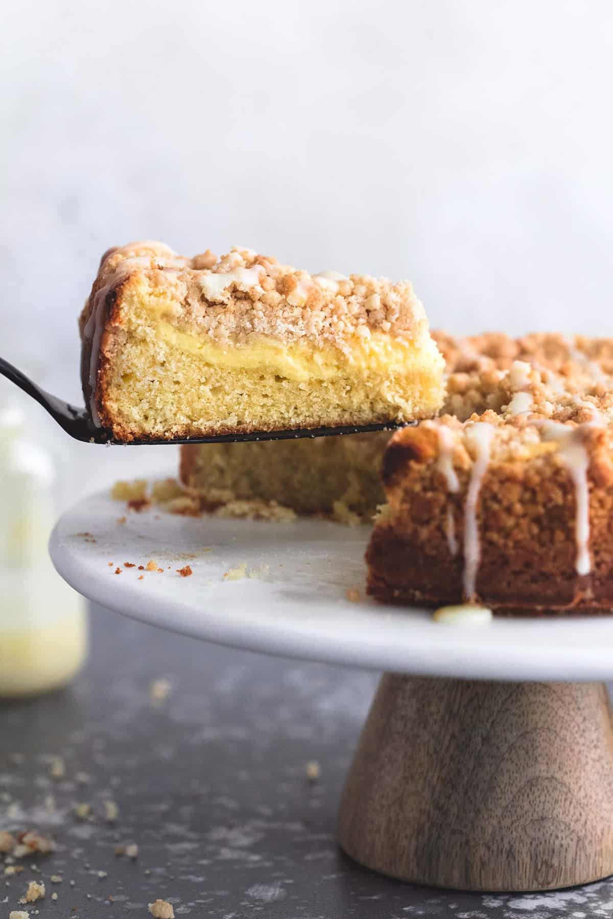 a spatula taking a piece of cream cheese lemon crumb cake on a cake stand.