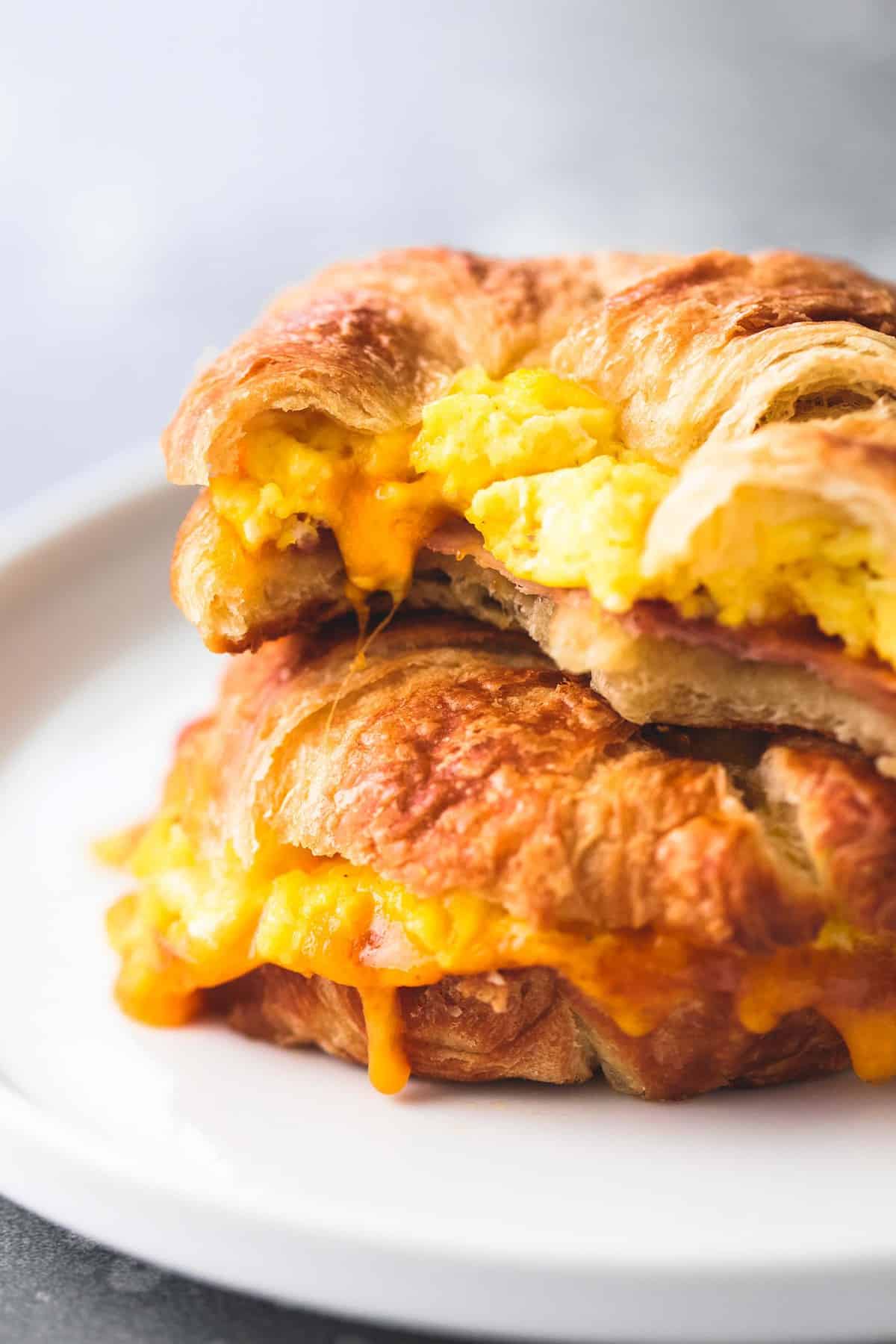 stacked baked croissant breakfast sandwiches on a plate with the top one missing a bite.