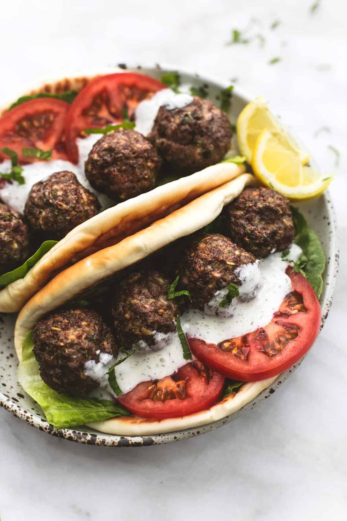 Greek meatballs in slices of flatbread with tomatoes, lettuce and sauce on a plate.