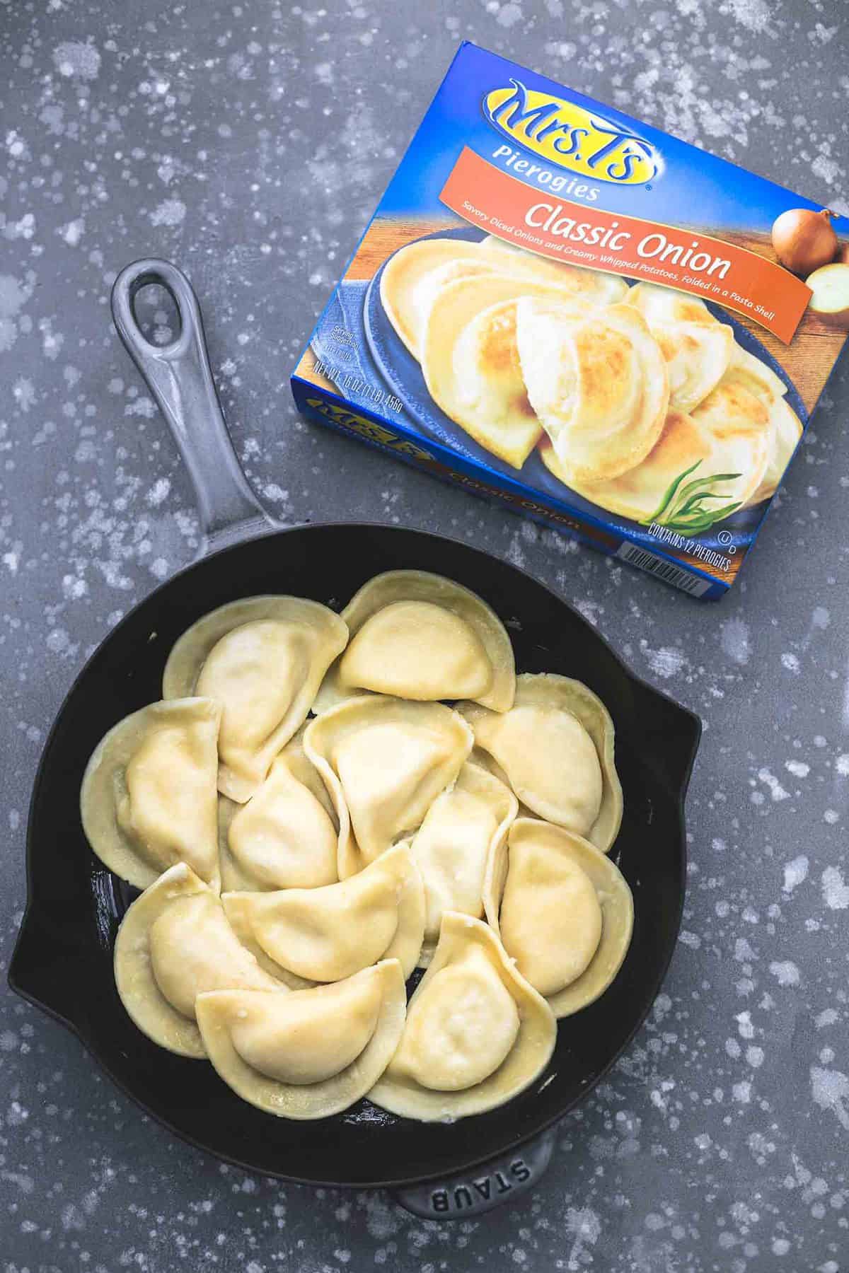 top view of pierogis uncooked in a skillet with a box of Mrs. T's pierogis on the side.
