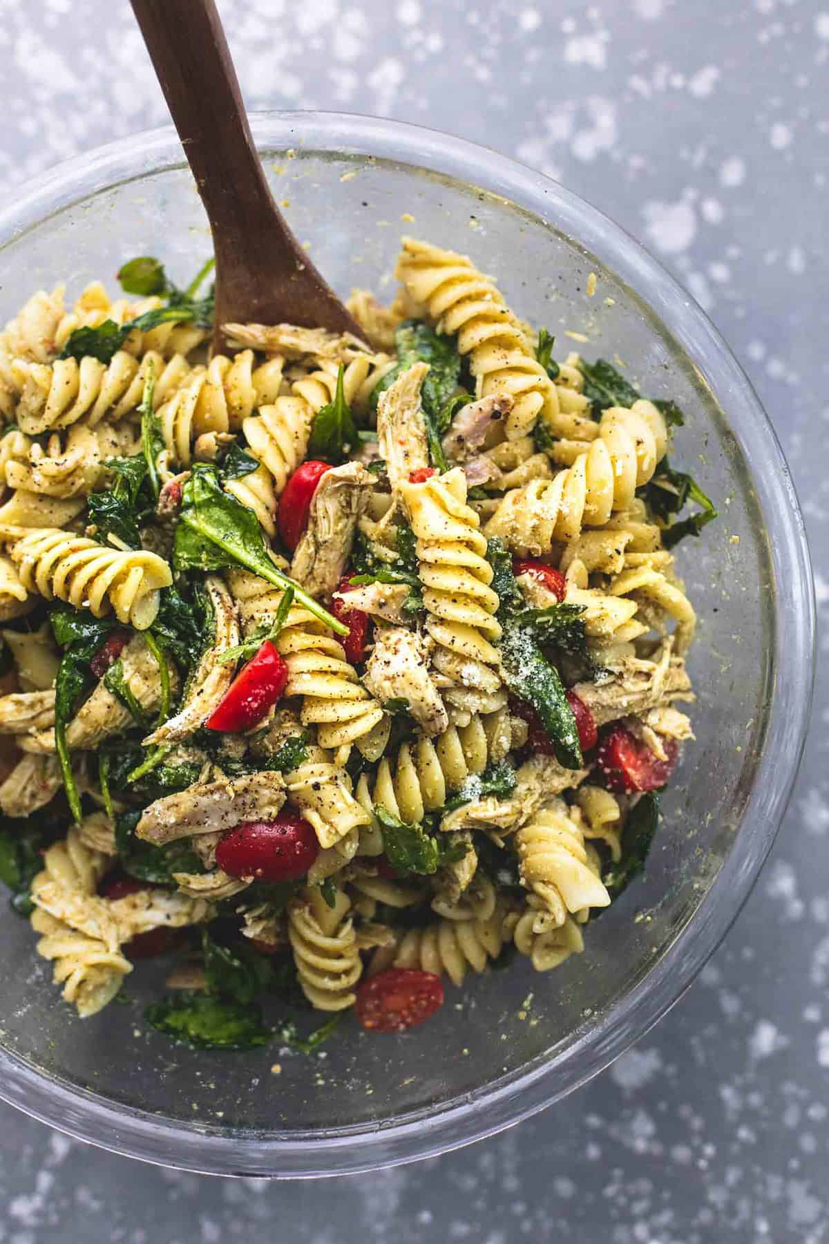 top view of pesto chicken pasta salad with a wooden serving spoon in a bowl.