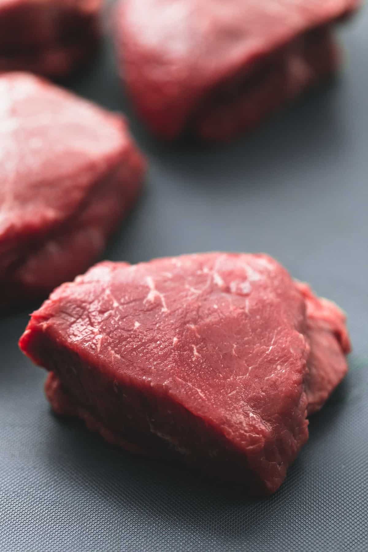 close up of a piece of steak uncooked with more raw pieces of steak in the background.
