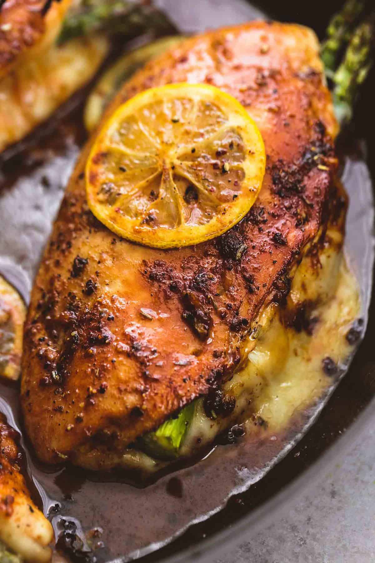 close up of a piece of asparagus stuffed chicken with more pieces of chicken on the side in a pan.