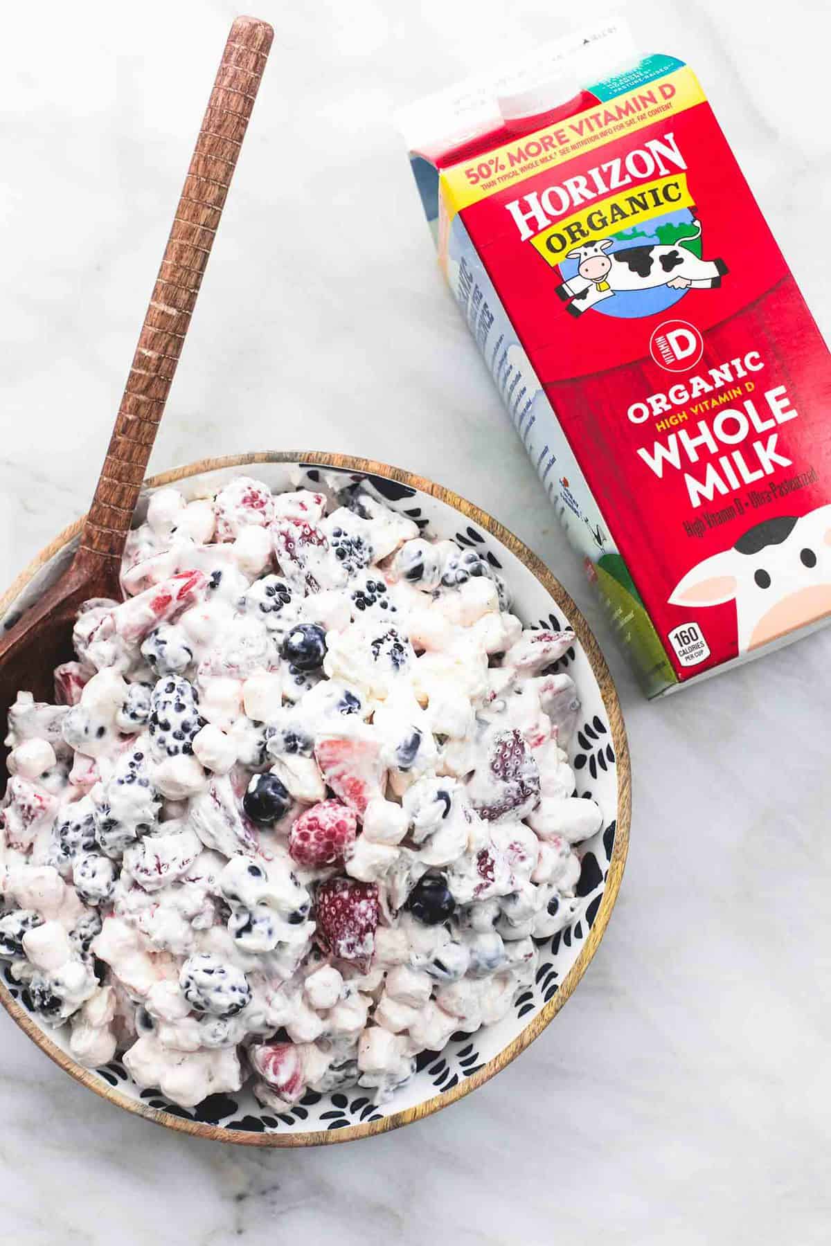 top view of berry cheesecake salad with a wooden serving spoon in a bowl with a carton of Horizon Organic whole milk on the side.