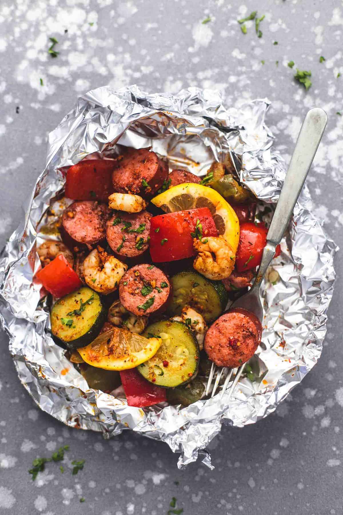 top view of a shrimp sausage and veggie foil pack with a fork.