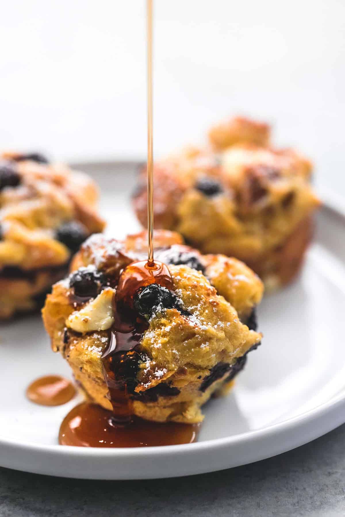 blueberry cream cheese French toast muffins on a plate with syrup being poured on the muffin in the front.