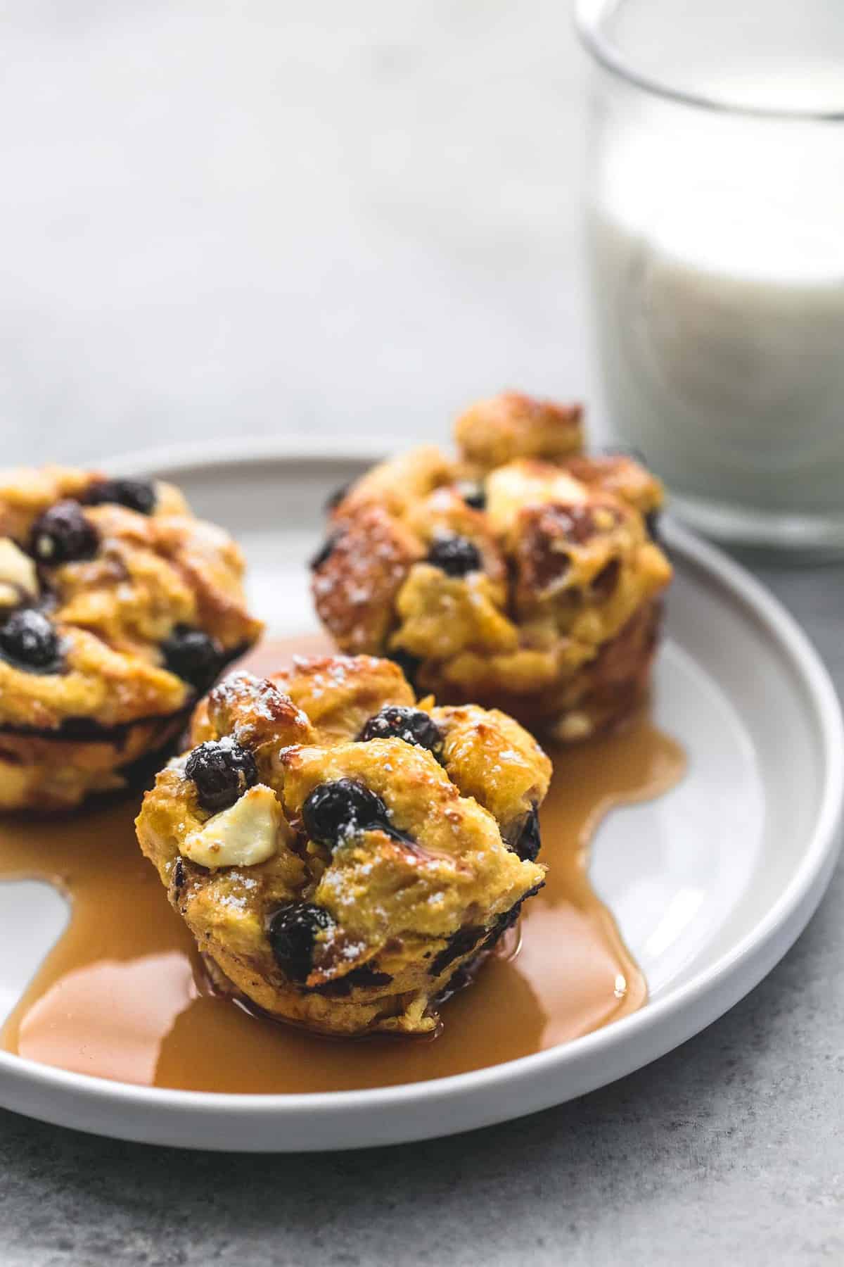 blueberry cream cheese French toast muffins topped with syrup on a plate with a glass of milk on the side.