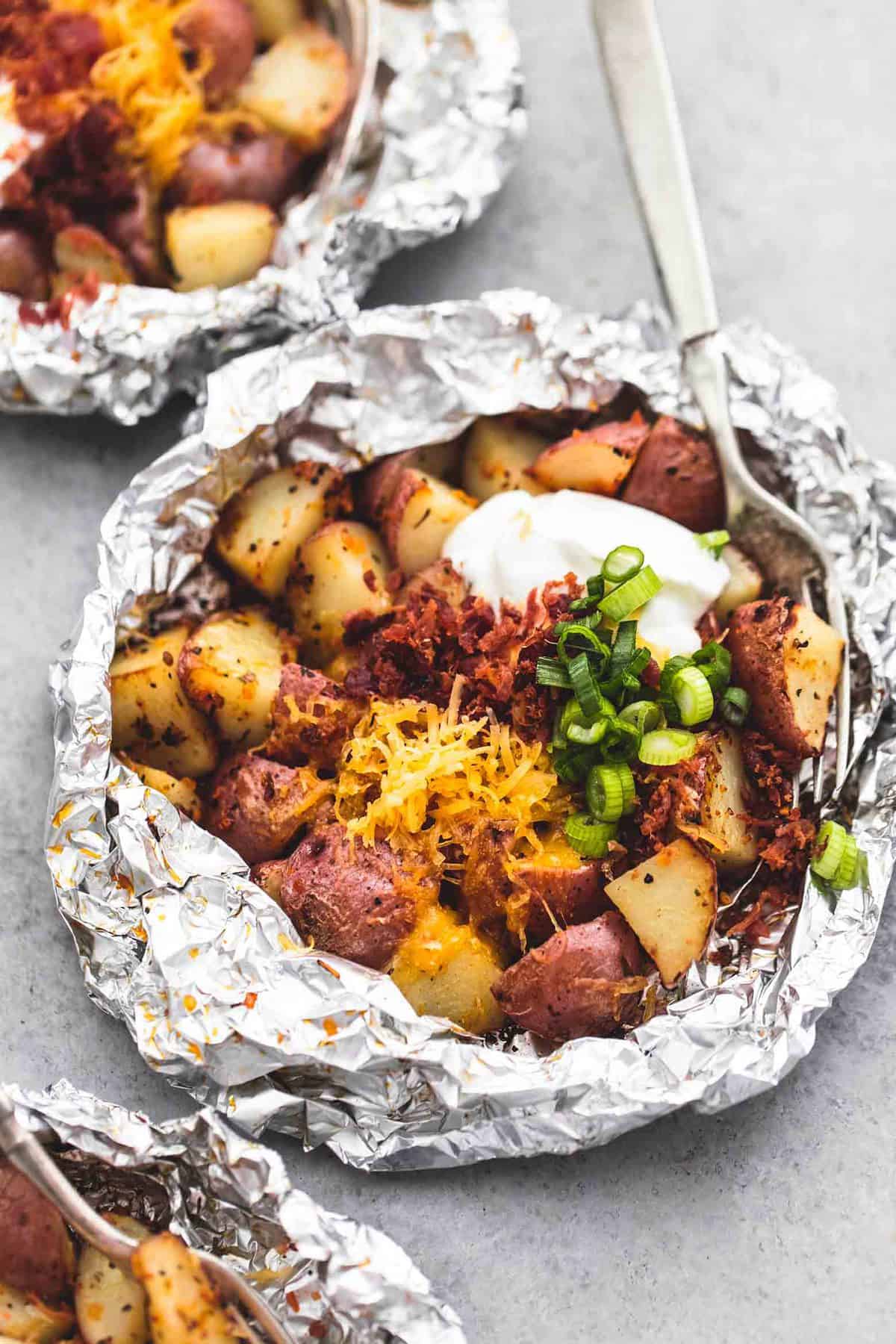 a loaded potato foil pack with a fork with more foil packs on the side.