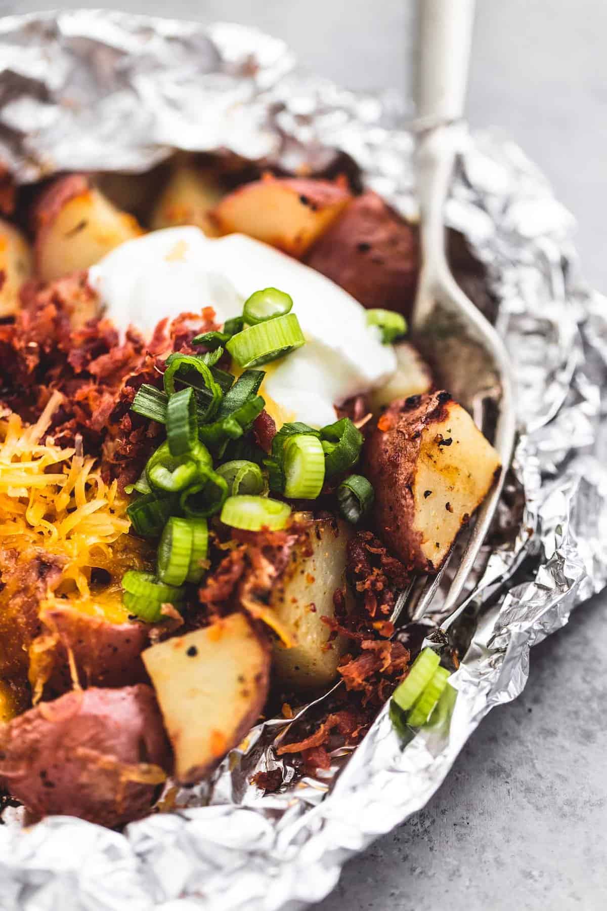 close up of a loaded potato foil pack with a fork.