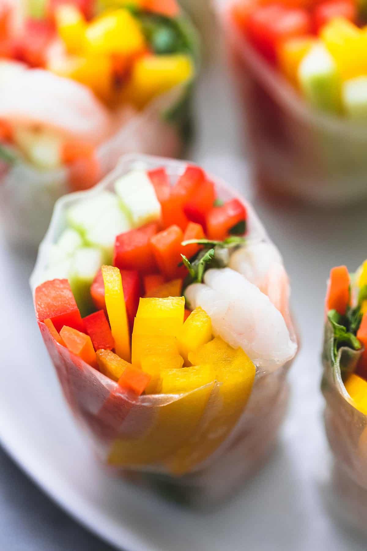 close up of a shrimp and veggie spring roll with more spring rolls on the side all on a plate.