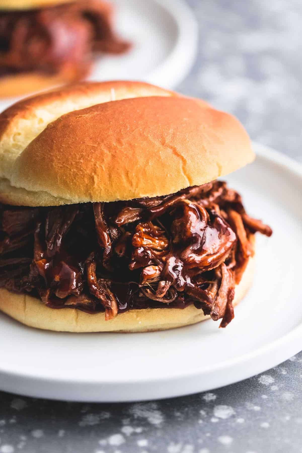 bbq pulled pork sandwich on a white plate on a gray tabletop.