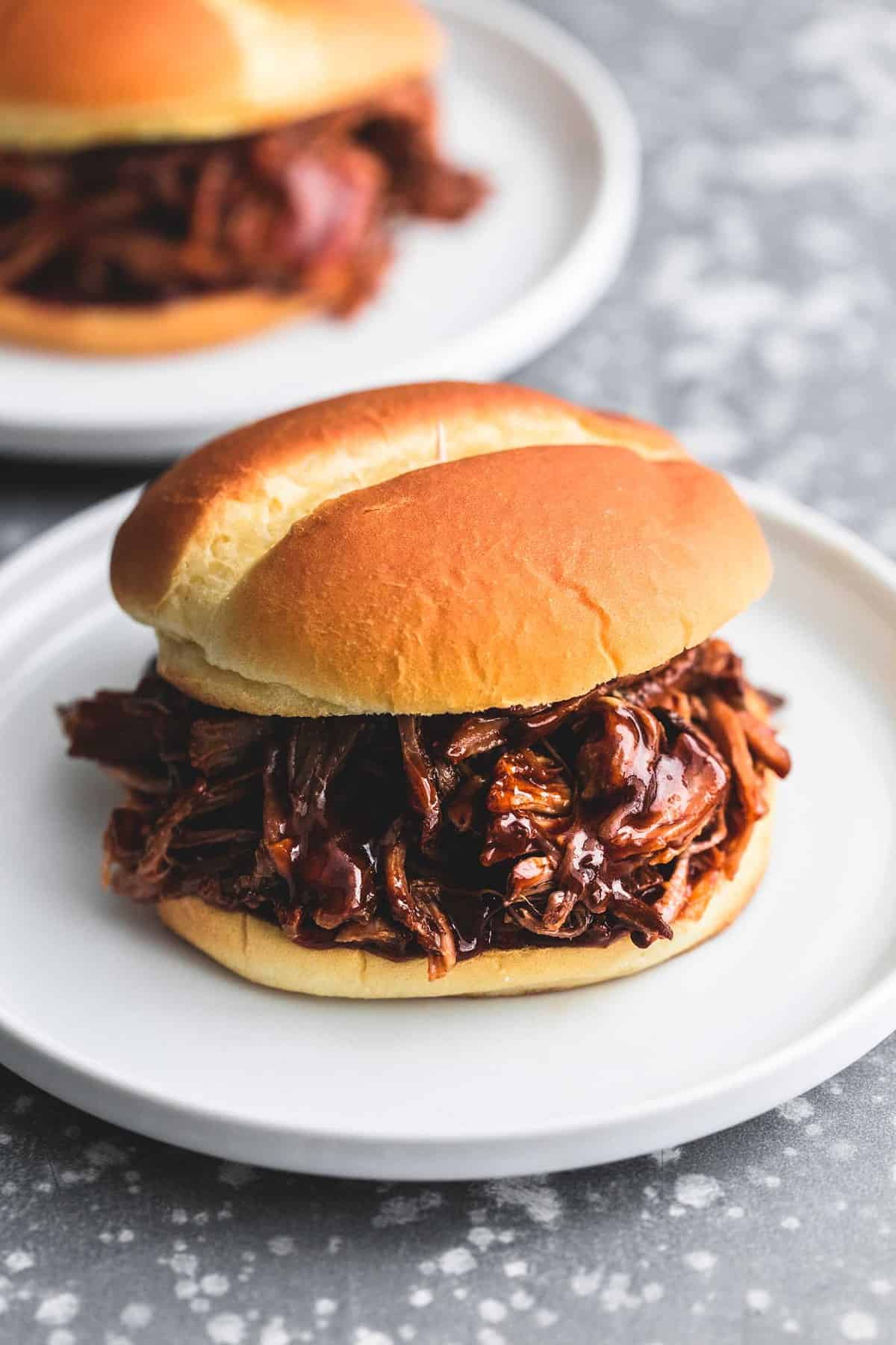up close view of a whole sandwich with pulled meat and bbq sauce in front of a second half-plate.