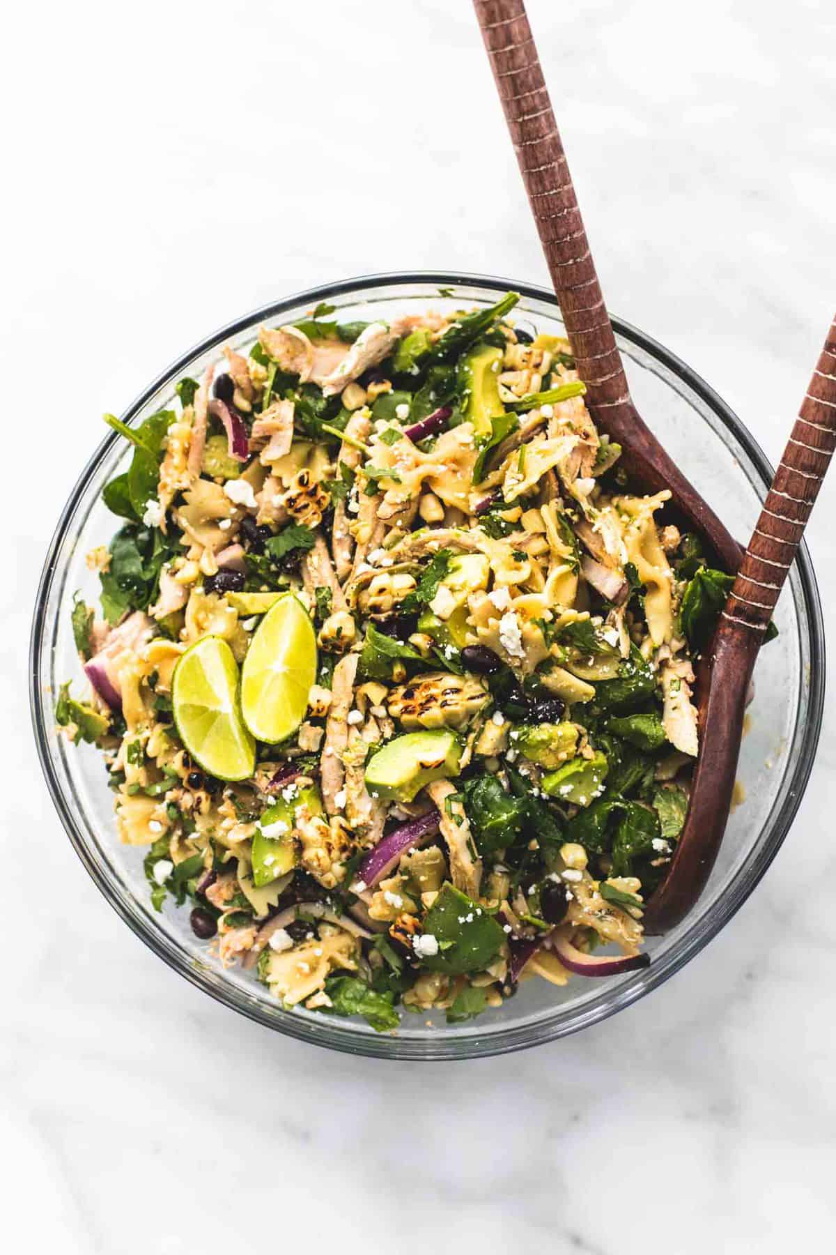 top view of Mexican street corn chicken pasta salad with two wooden serving spoons in a glass bowl.