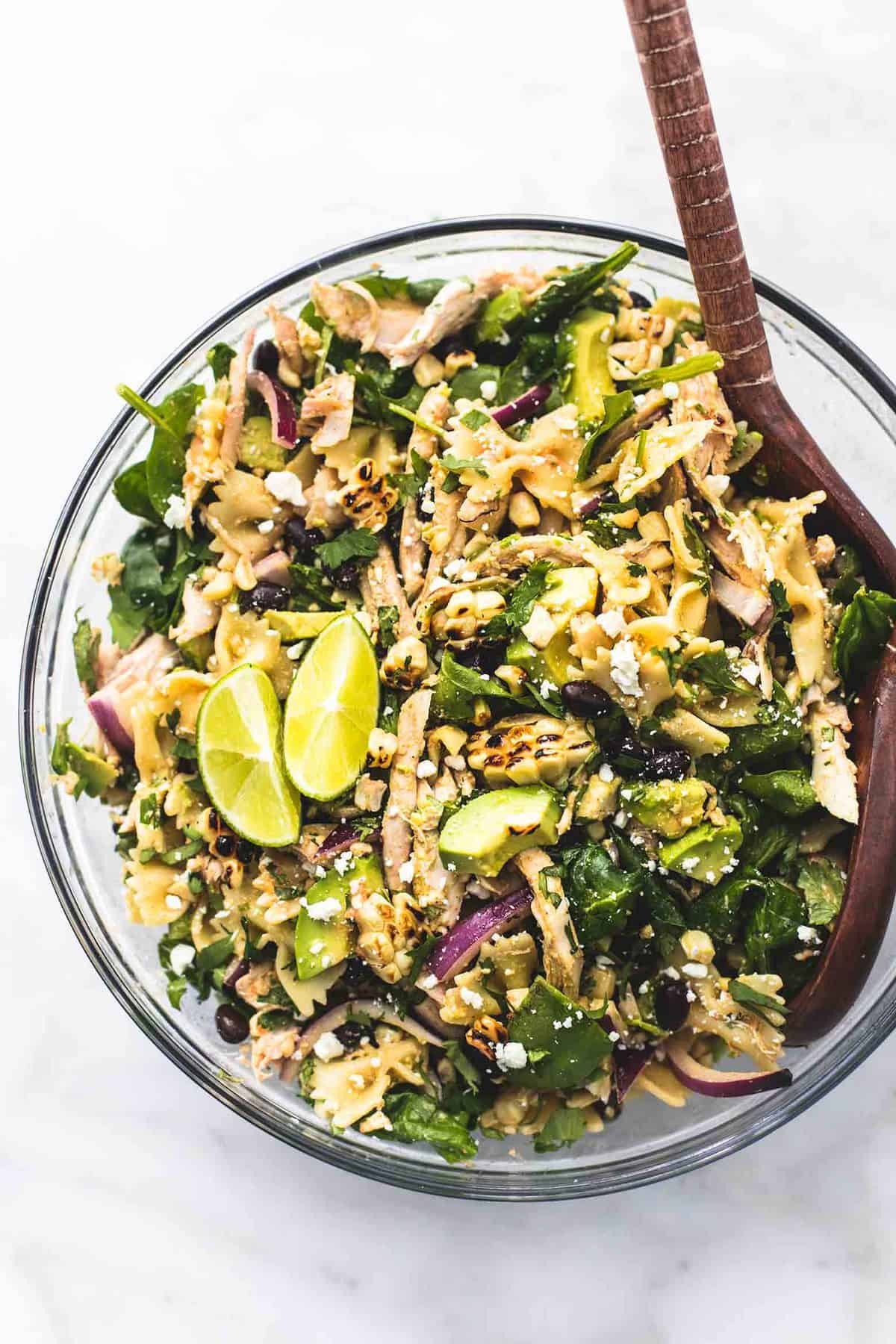 top view of Mexican street corn chicken pasta salad with two wooden serving spoons in a glass bowl.