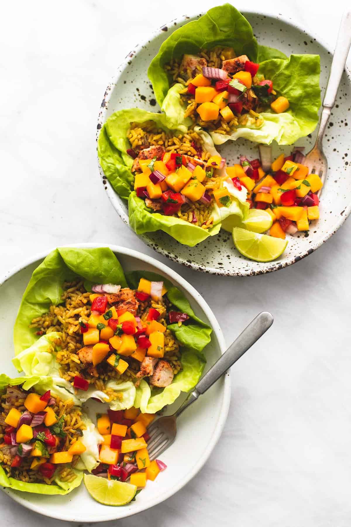 top view of two plates with Caribbean chicken and rice lettuce wraps and forks on them.