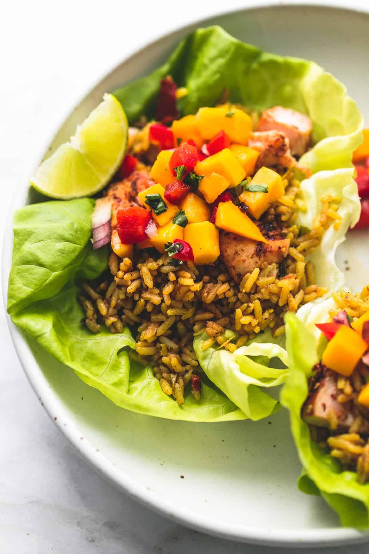 close up of a Caribbean chicken and rice lettuce wrap with another one on the side all on a plate.