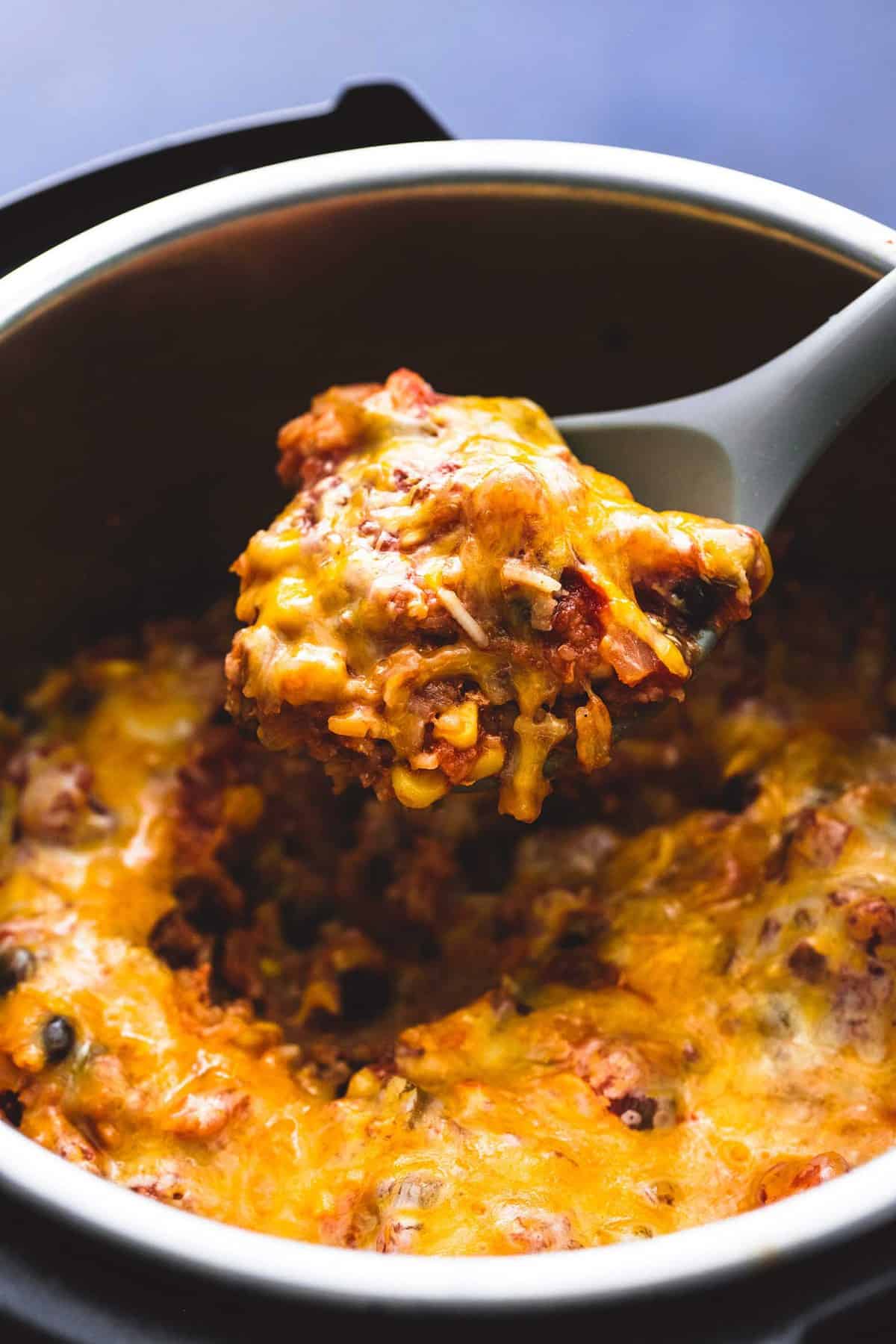 close up of a serving spoon with a scoop of instant pot cheesy Mexican chicken and rice on it being held above an instant pot of more chicken and rice.