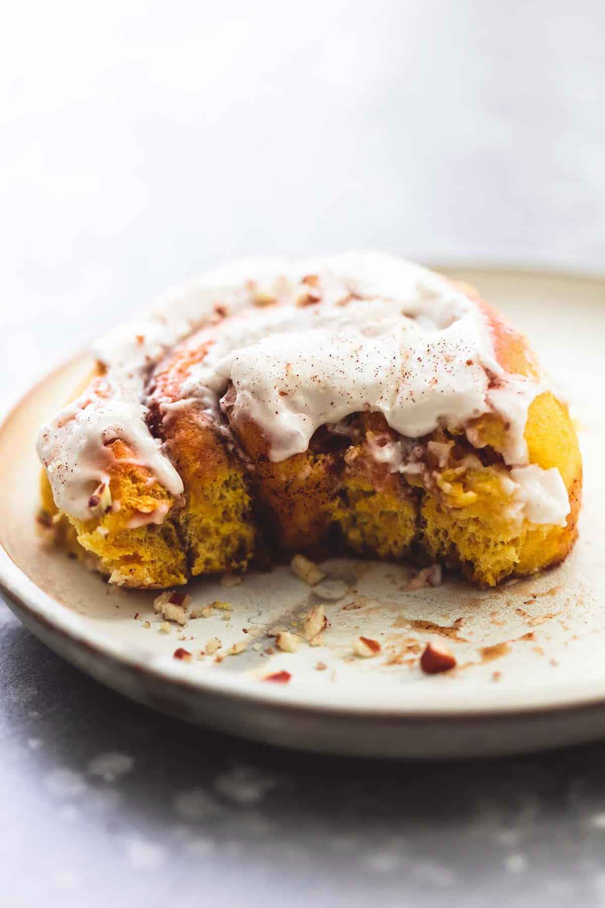 a pumpkin cinnamon roll missing a bite on a plate.