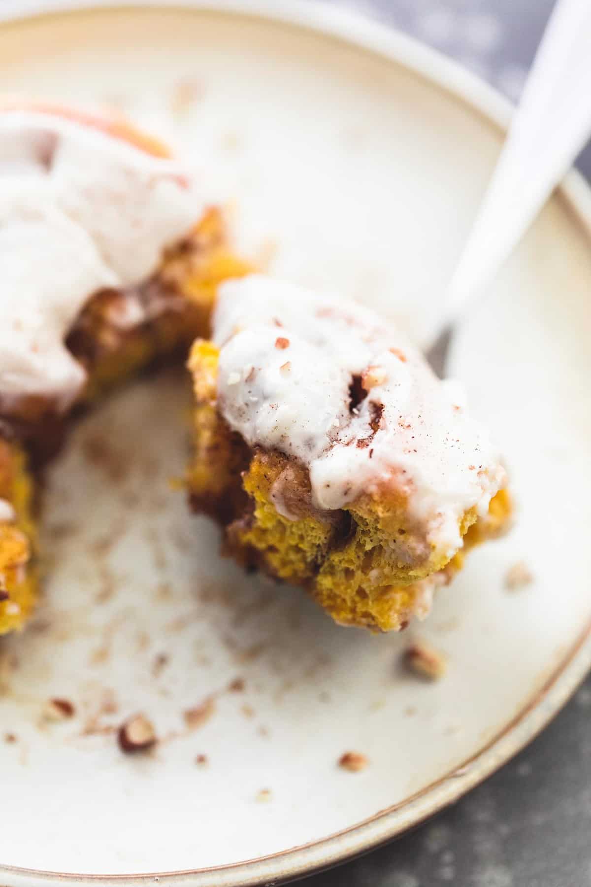 close up of a bite of a pumpkin cinnamon roll on a fork next to the rest of the roll on a plate.