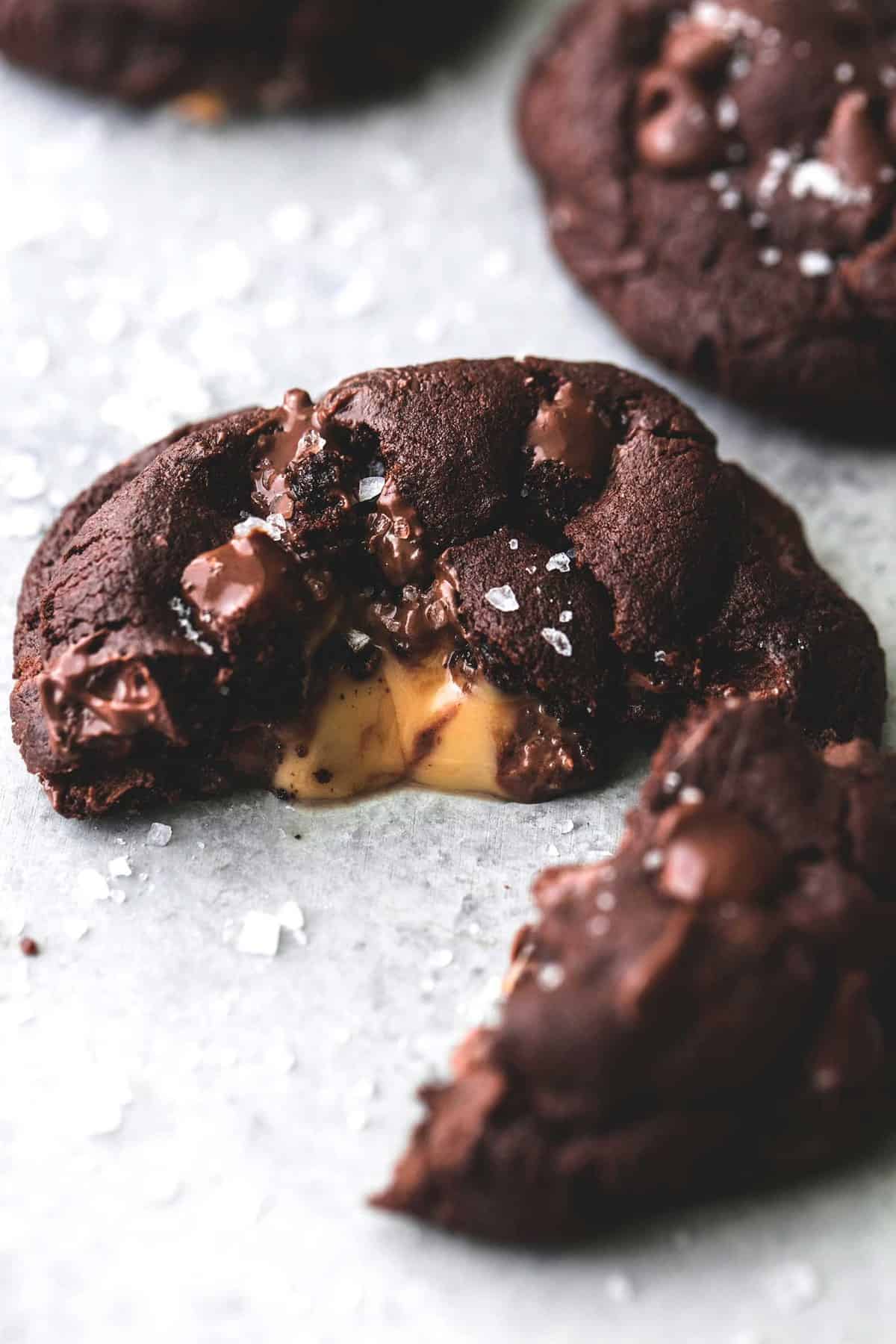 close up of a salted caramel stuffed double chocolate cookie broken in half to show the middle.