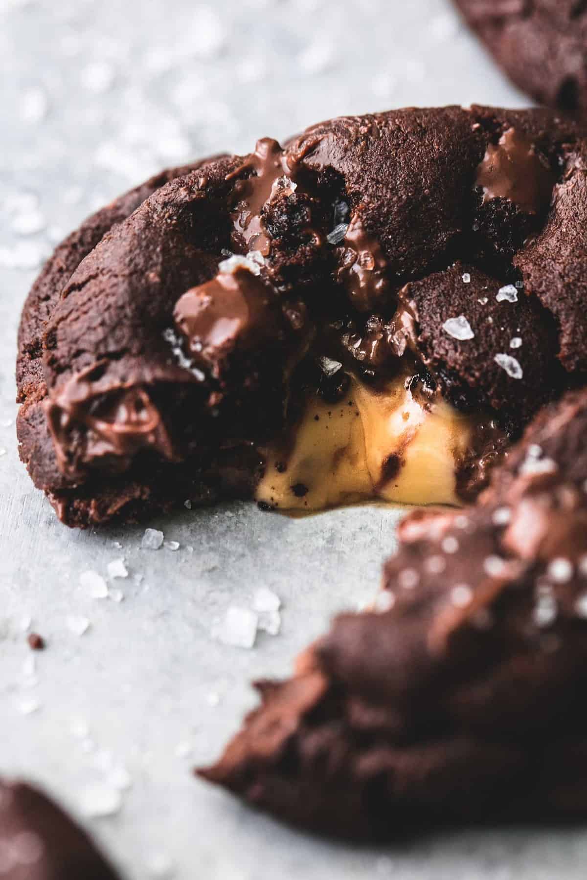 close up of a salted caramel stuffed double chocolate cookie broken in half to show the caramel in the middle.