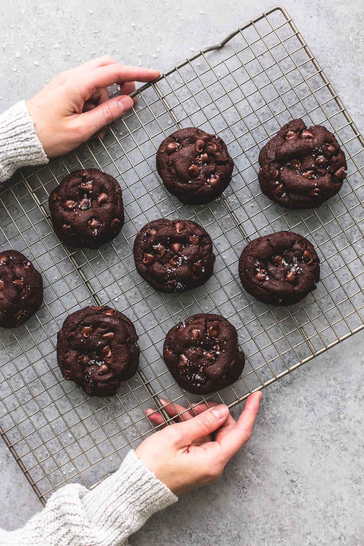 top view of a pair of hands holding a cooling rack with salted caramel stuffed double chocolate cookies on it.