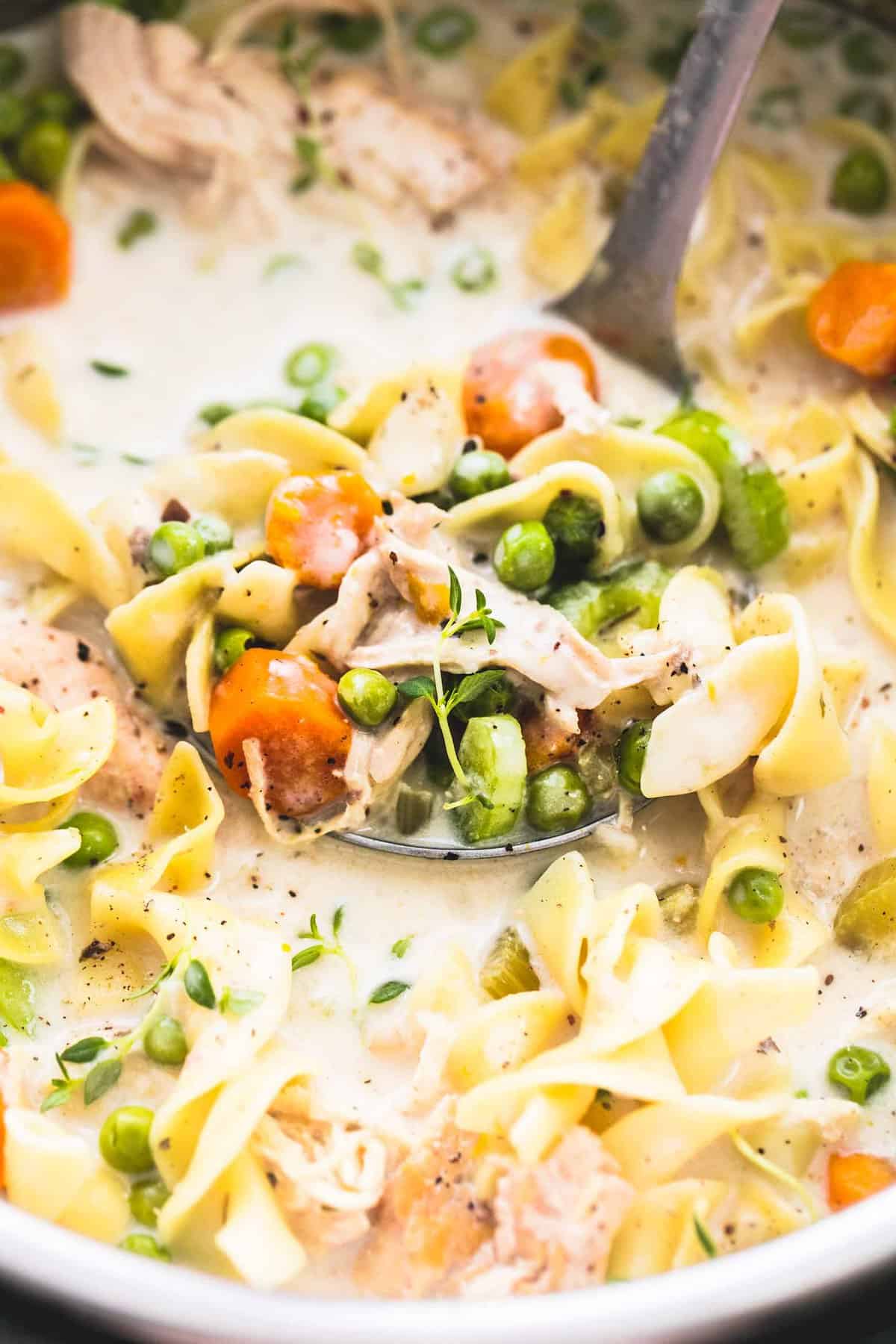 close up of creamy chicken noodle soup with a scoop on a serving spoon.