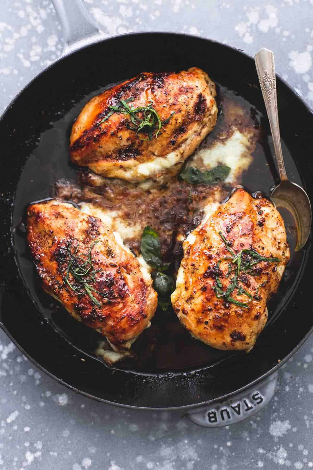 top view of three cheese stuffed balsamic chicken with a spoon in a skillet.