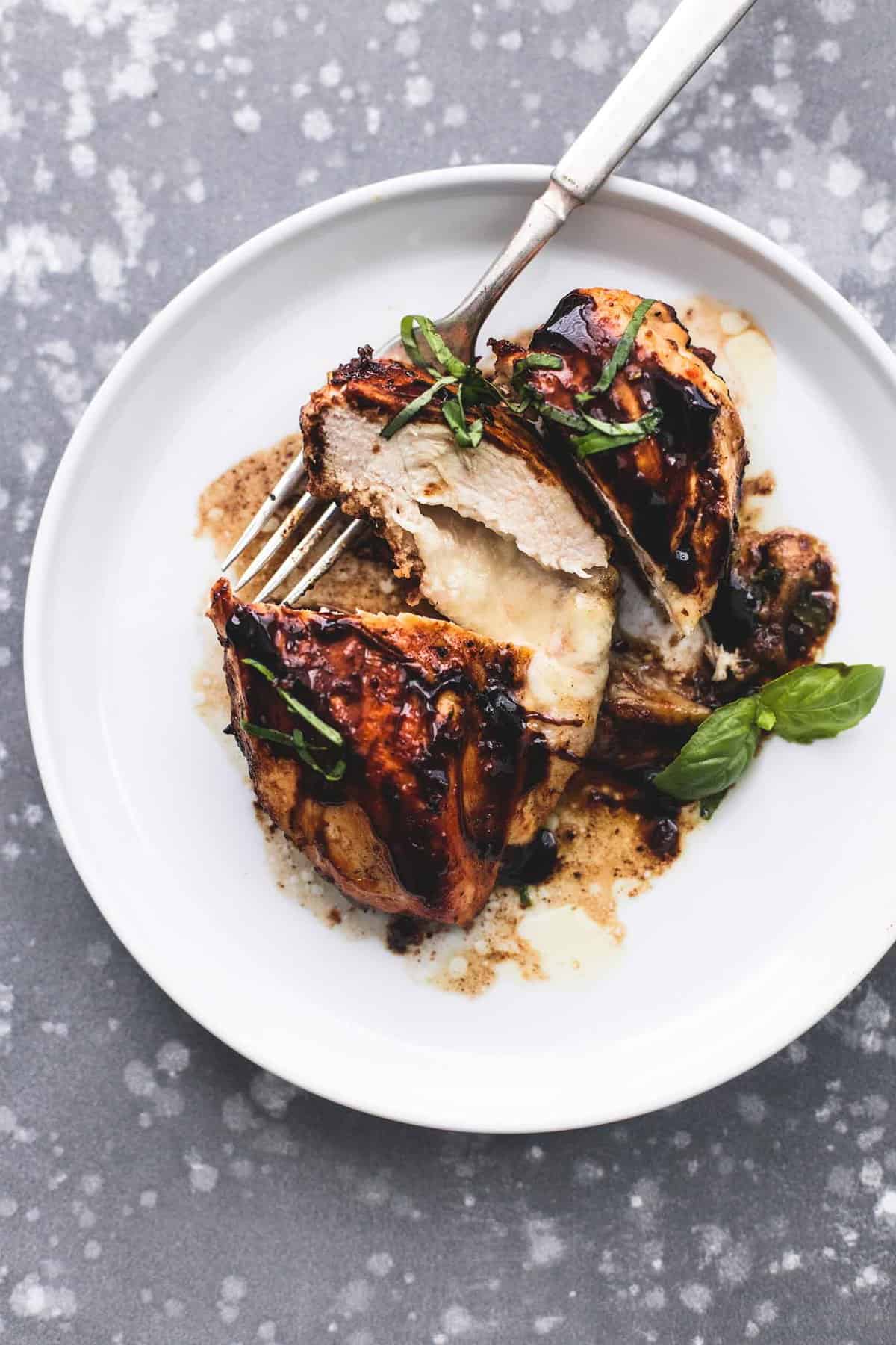 top view of three cheese stuffed balsamic chicken sliced up with a fork underneath on a plate,
