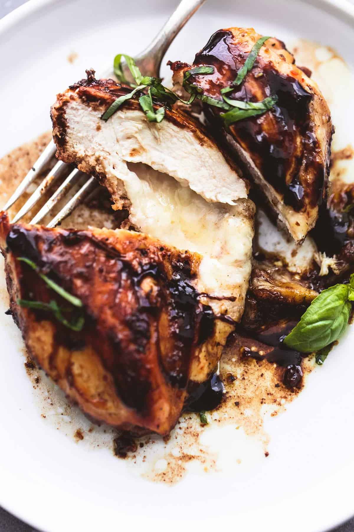 close up of three cheese stuffed balsamic chicken sliced up with a fork underneath on a plate.