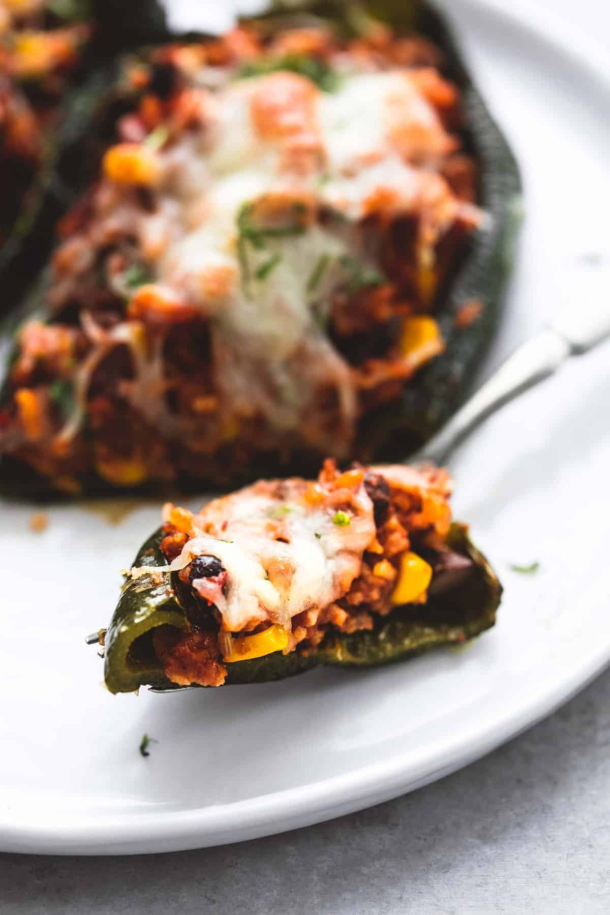 close up of a bite of Southwest stuffed poblano peppers on a fork with stuffed peppers in the background all on a plate.