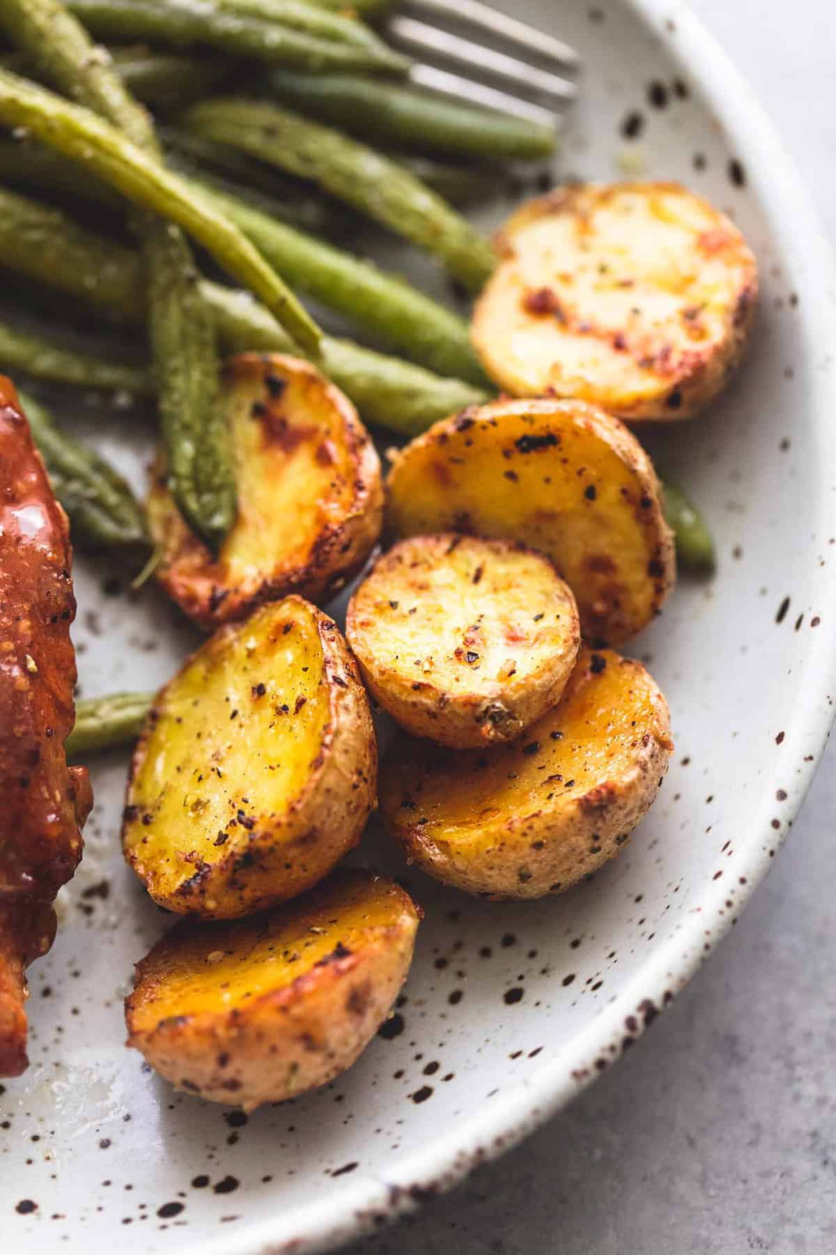 close up of potatoes with green beans and chicken on the side all on a plate.