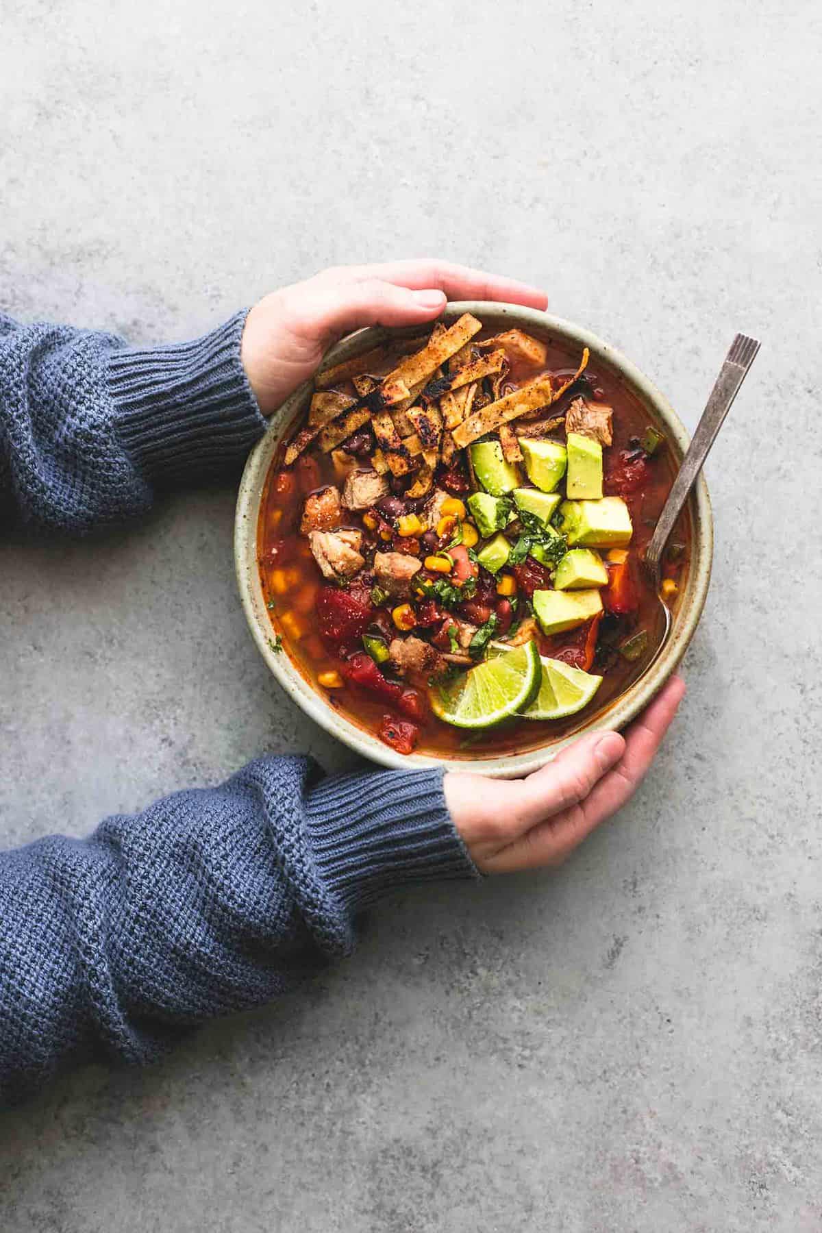 top view of a pair of hands holding a bowl of Mexican chicken tortilla soup with a spoon.